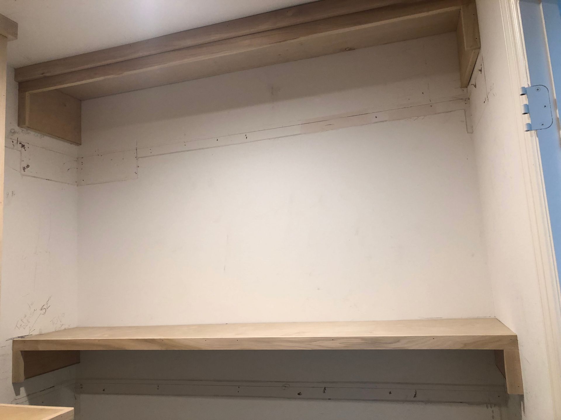 Two unfinished light wood shelves installed in a white wall alcove, with visible mounting brackets and wall markings.
