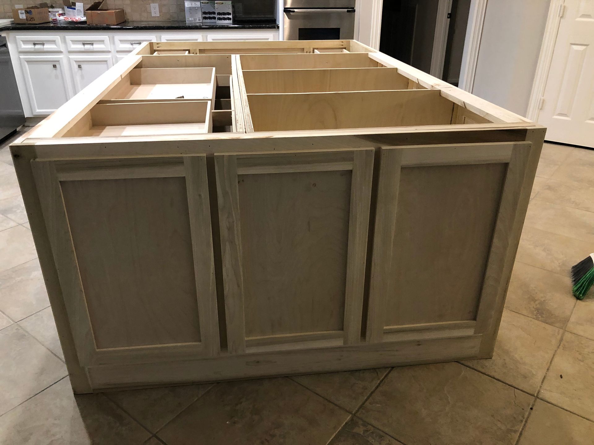 A large, unfinished wooden kitchen island with built-in drawer compartments sitting on a tiled floor.