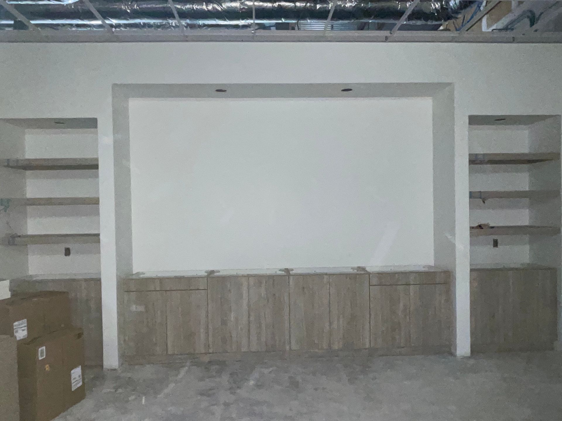A custom wall unit with a large central recess for a TV, flanked by wooden shelves and base cabinets in a room under repair.