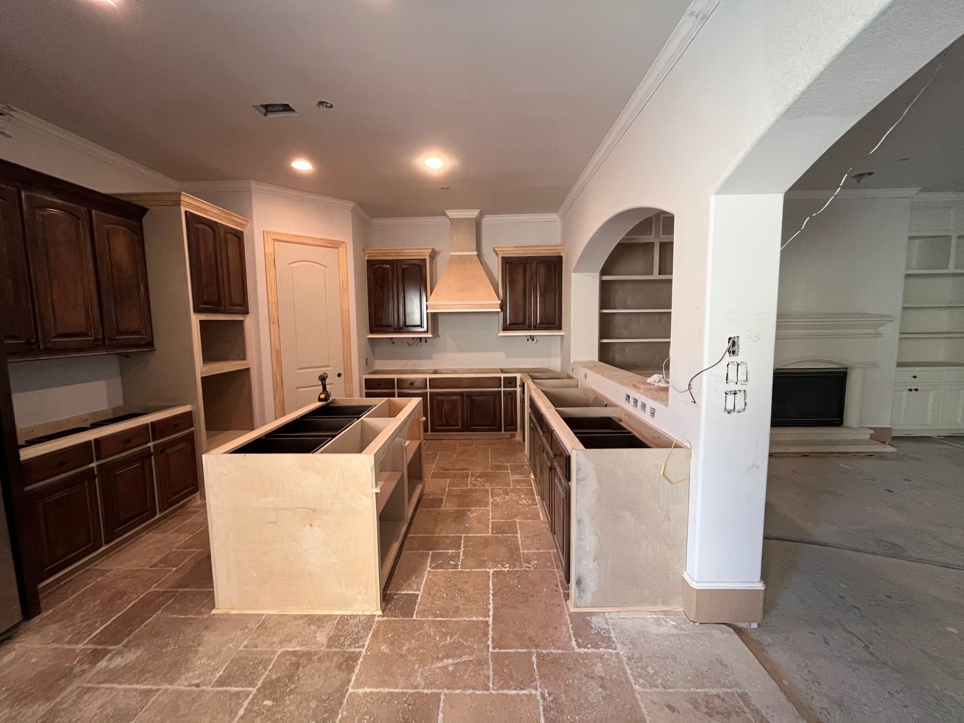A kitchen under renovation featuring dark wood cabinets, a central island, and unfinished stone flooring.