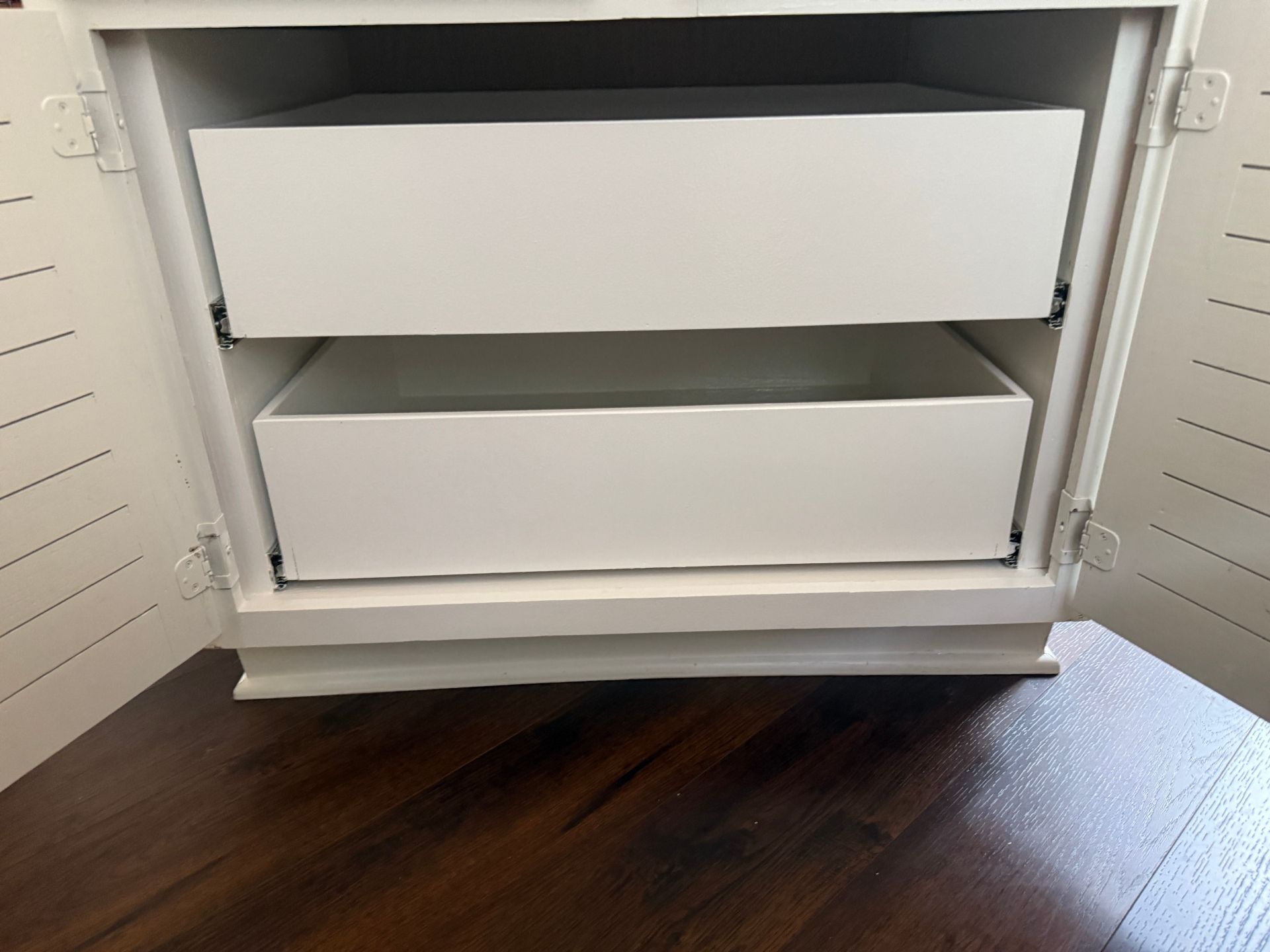 Two white, empty drawers open inside a white cabinet frame sitting on a dark wooden surface.