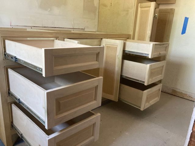 Unfinished wooden cabinet with several open drawers pulled out in a room under construction.