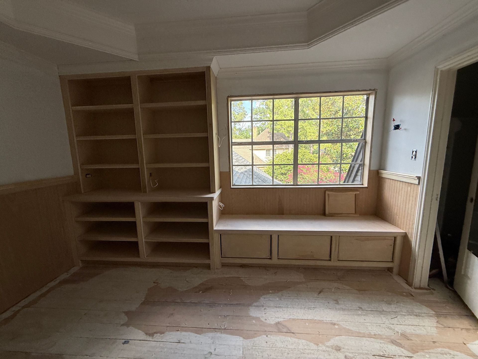 Unfinished built-in wooden shelving and a window seat with storage compartments in a room under construction.