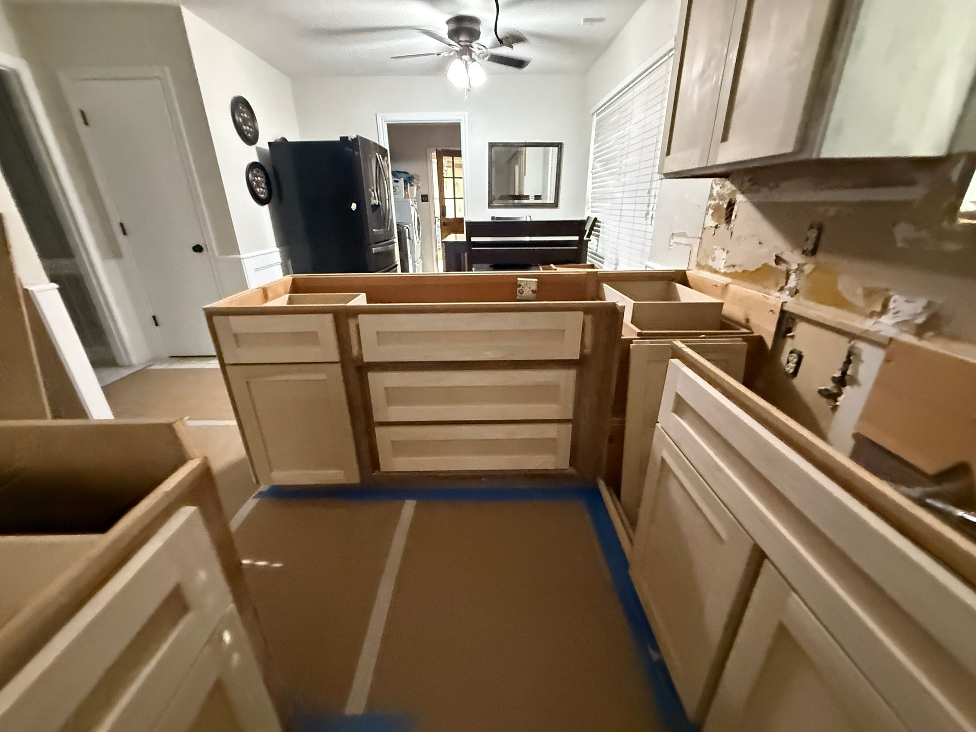 An unfinished kitchen renovation featuring light-colored wooden cabinets installed in a room with a ceiling fan.