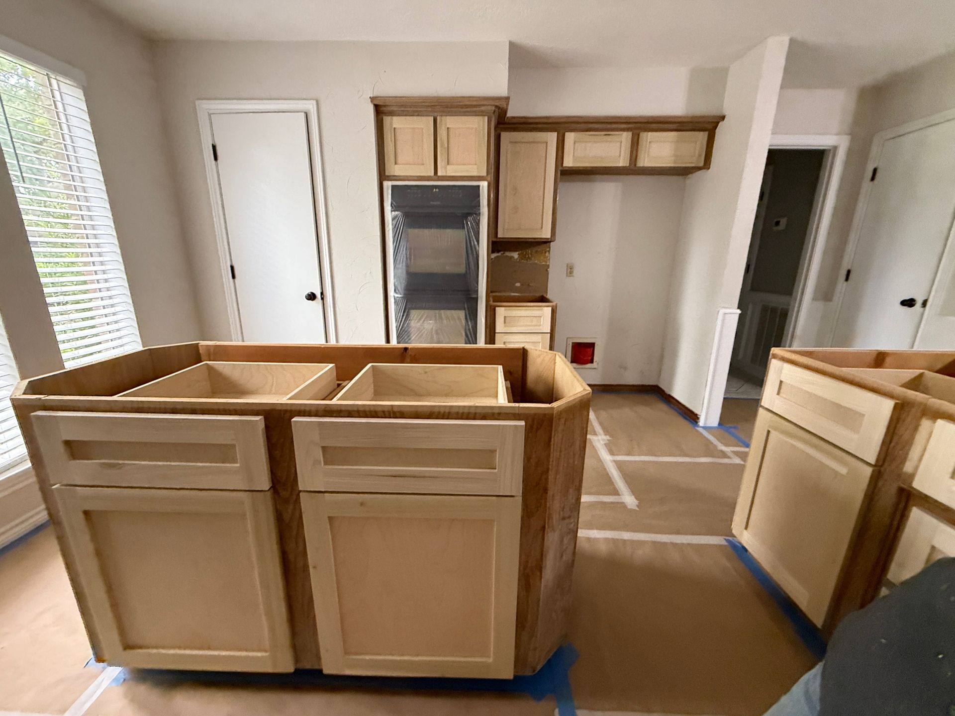 A kitchen undergoing renovation with light wood cabinets and an island installed on a floor covered with protective paper.