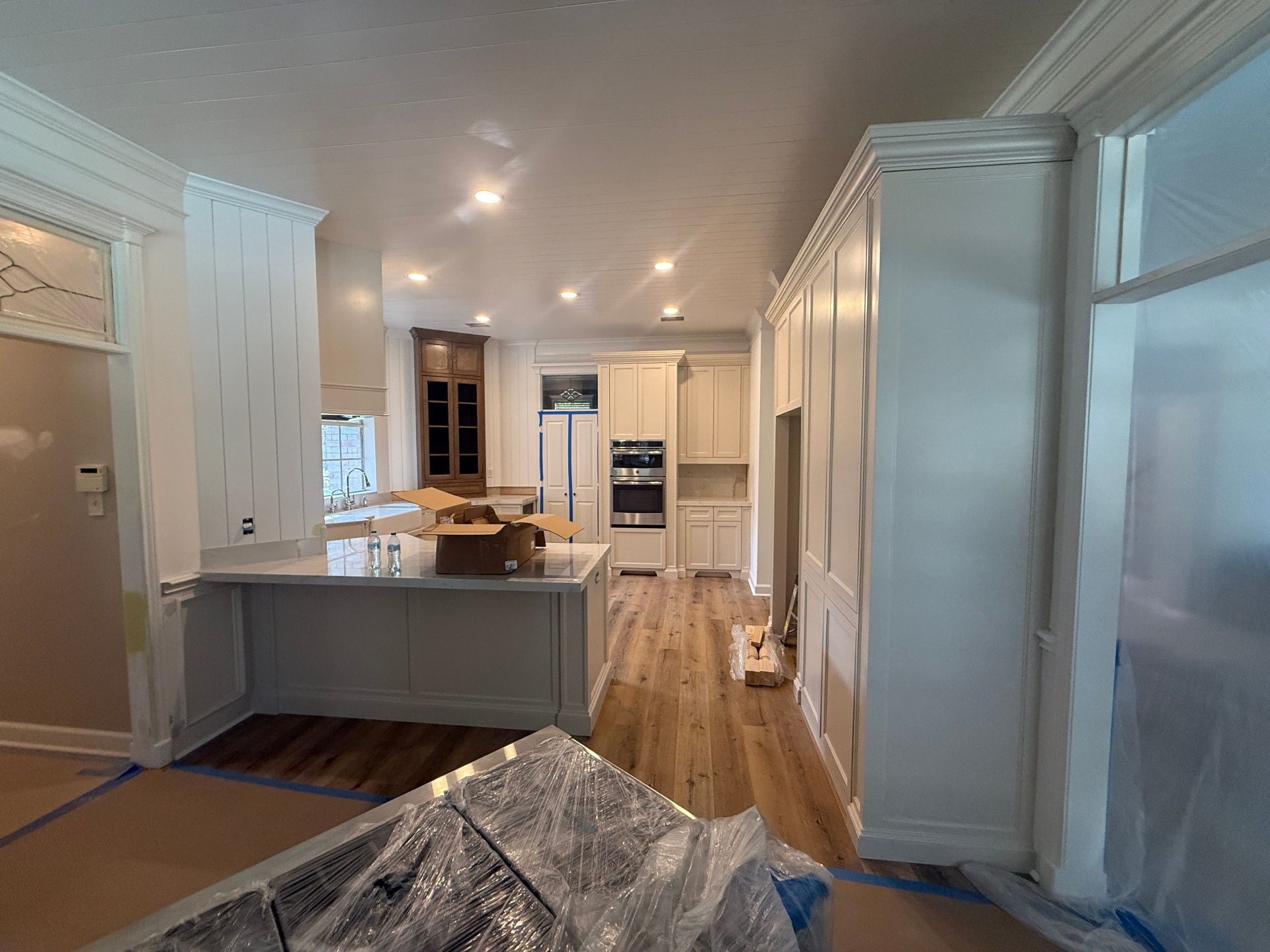 A kitchen under construction featuring white cabinetry, light wood floors, an island, and plastic-covered surfaces.
