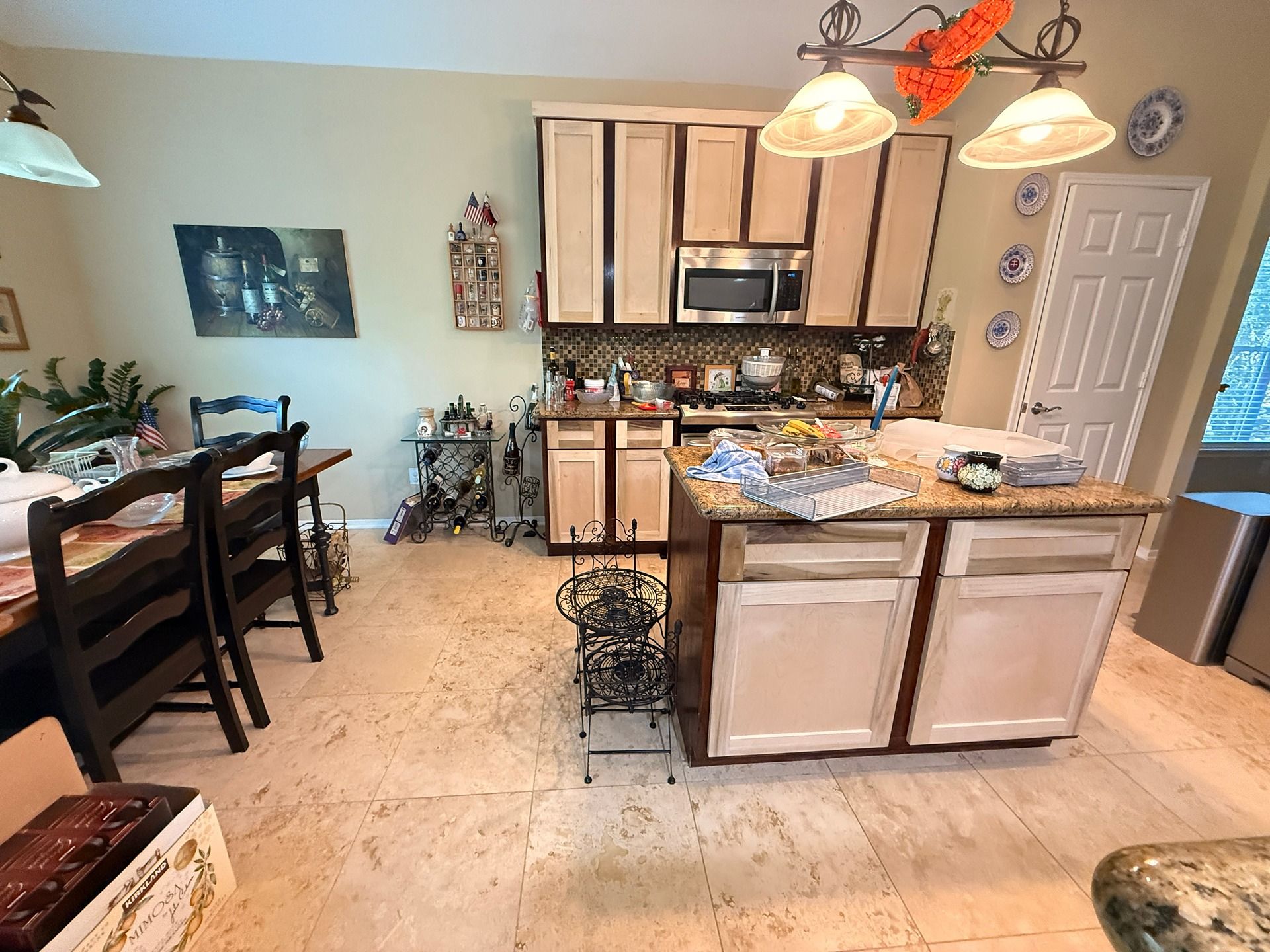 A brightly lit kitchen with cream cabinets, a central island, and a dining table set to the left.