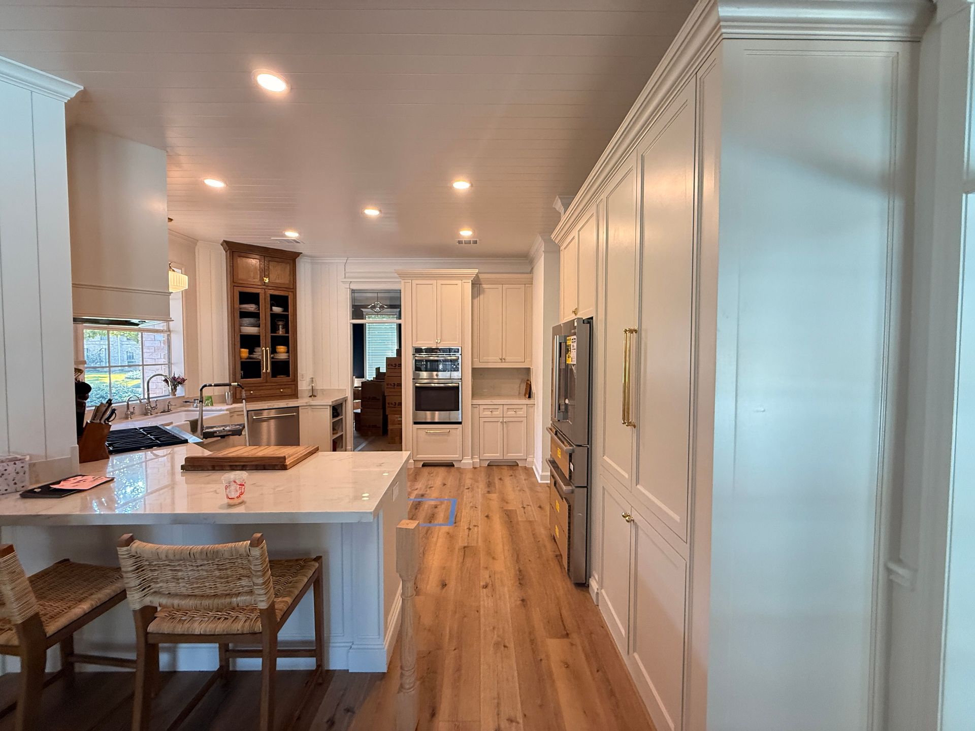 A modern, brightly lit white kitchen with a large central island, light wood floors, and a double wall oven.