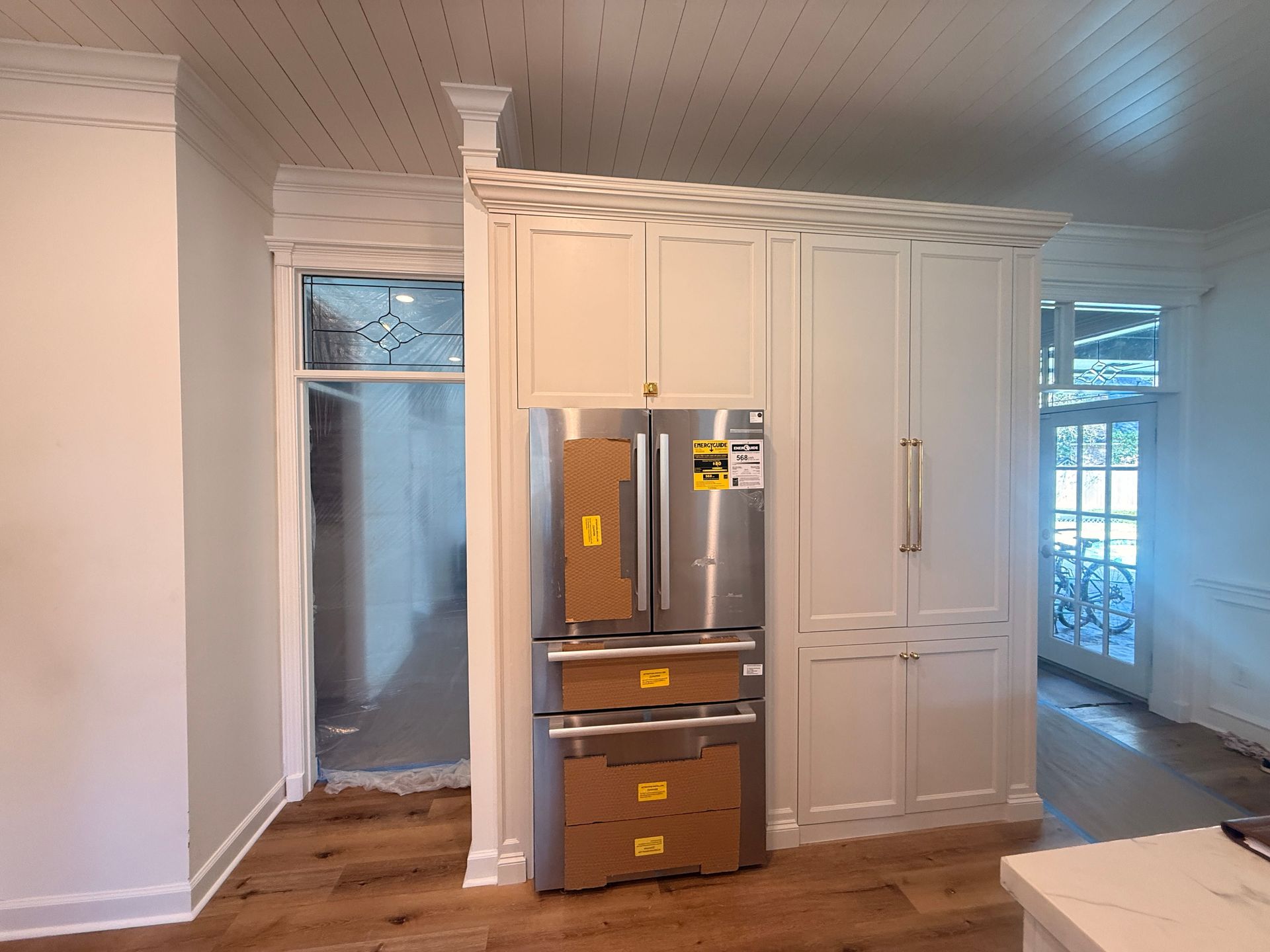 A modern kitchen features a built-in stainless steel refrigerator next to floor-to-ceiling white cabinets under crown trim.
