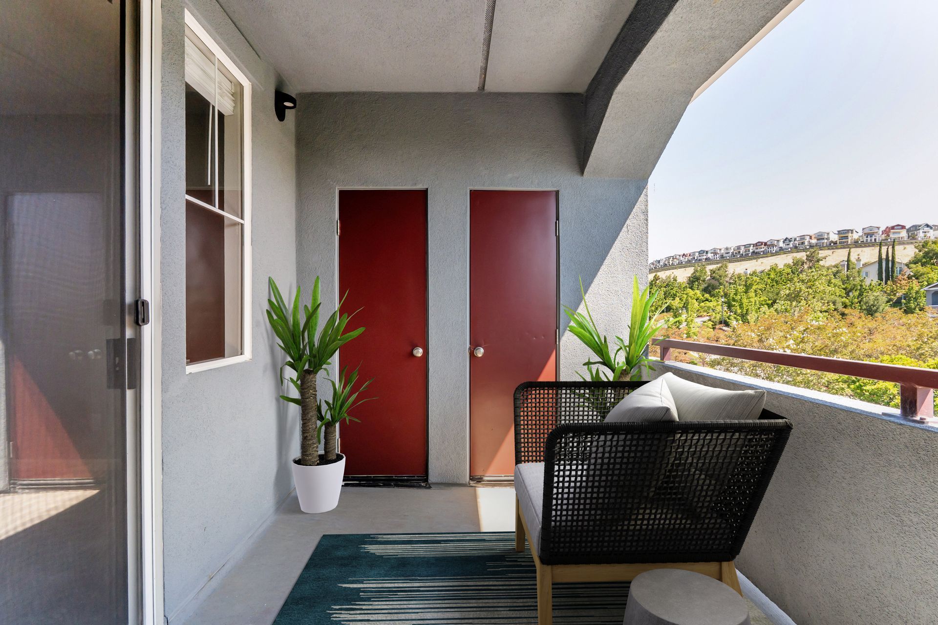 Balcony with red doors, potted plants, and a black chair overlooking greenery