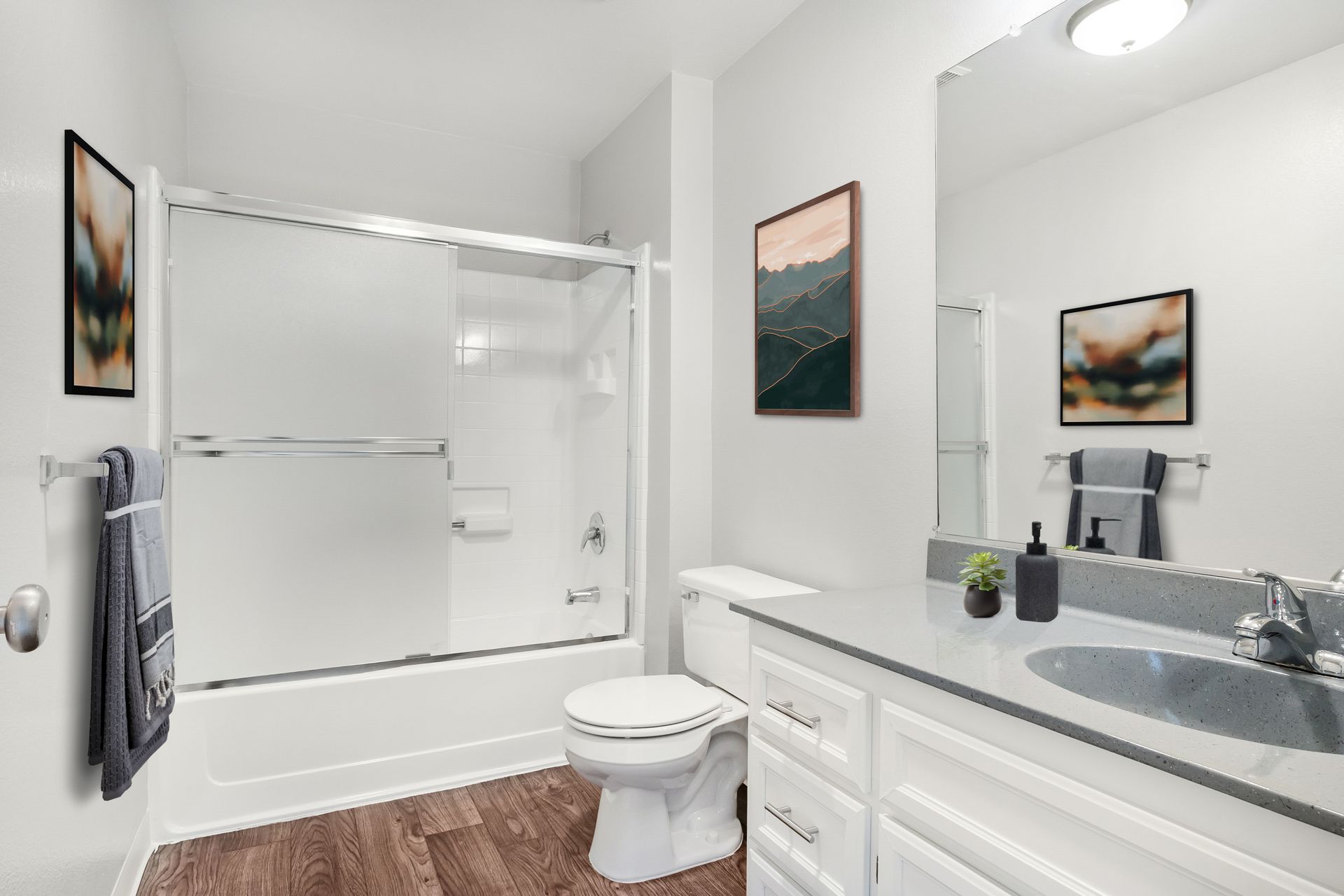 Bright bathroom with white vanity, toilet, bathtub shower, gray walls, and framed wall art