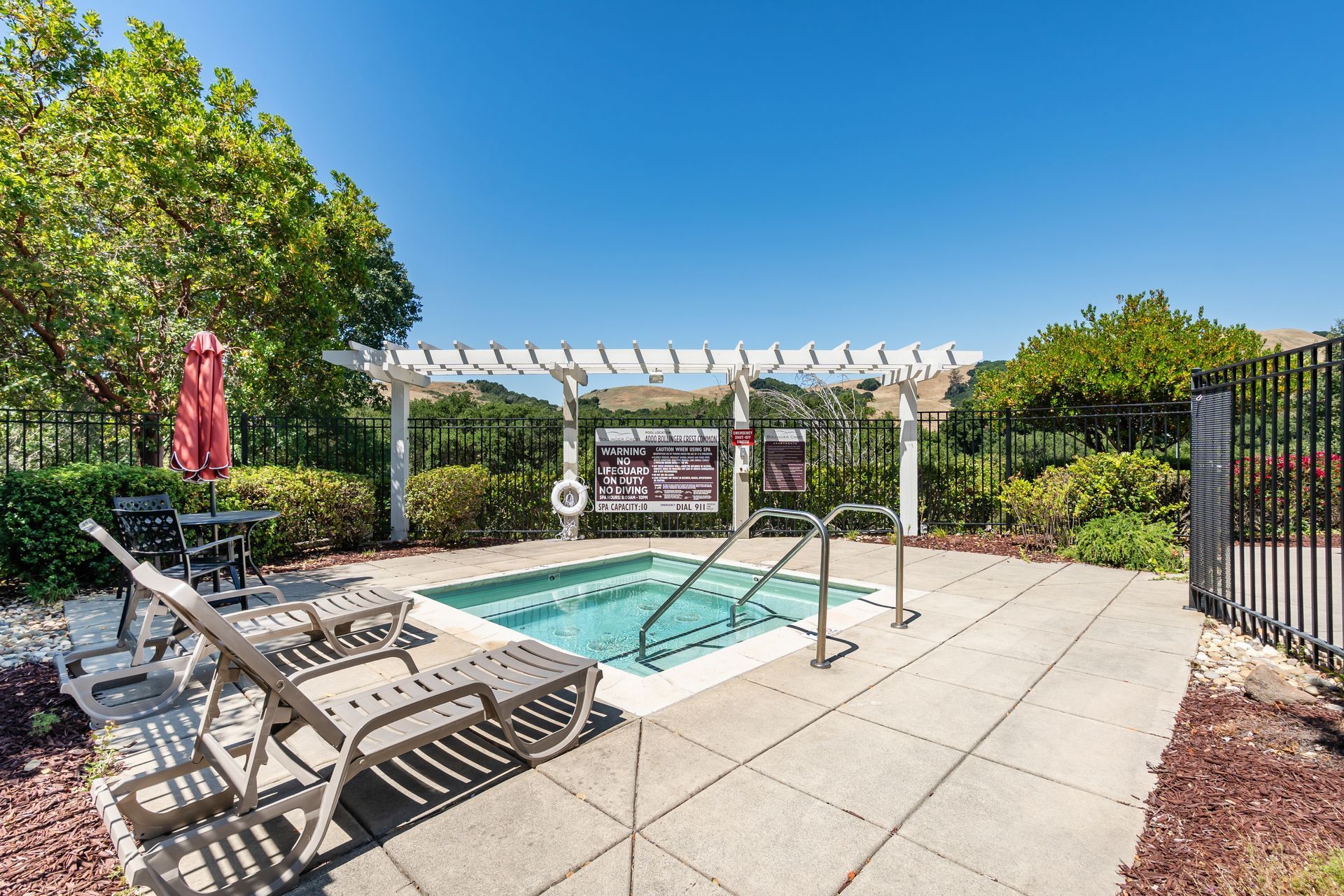 Sunny outdoor pool with lounge chairs, white pergola, and patio seating in a landscaped courtyard