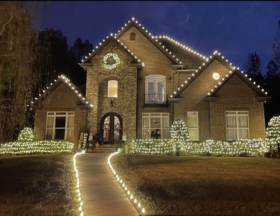 Brick house outlined with white holiday lights at night, with a lit walkway leading to the front door