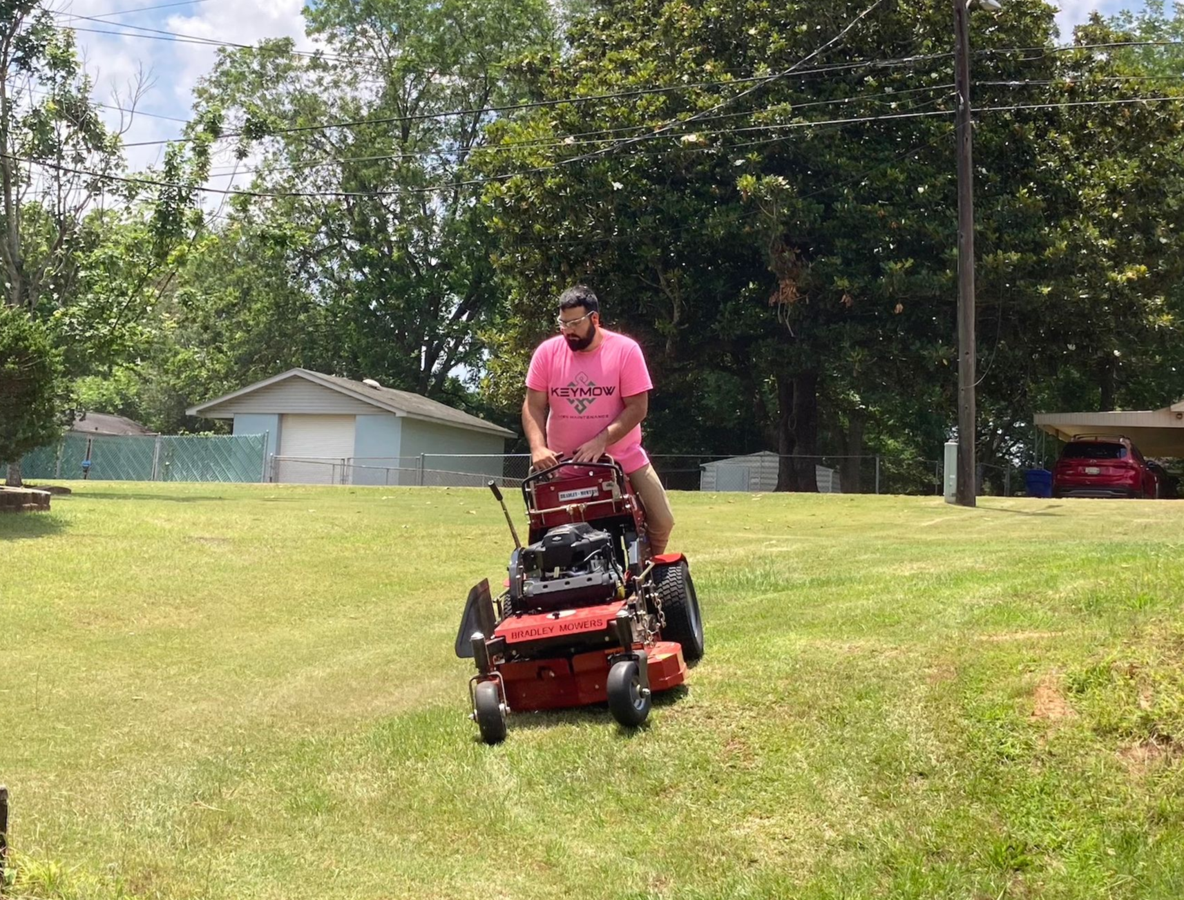 Person mowing a grassy lawn on a red riding mower in a sunny yard