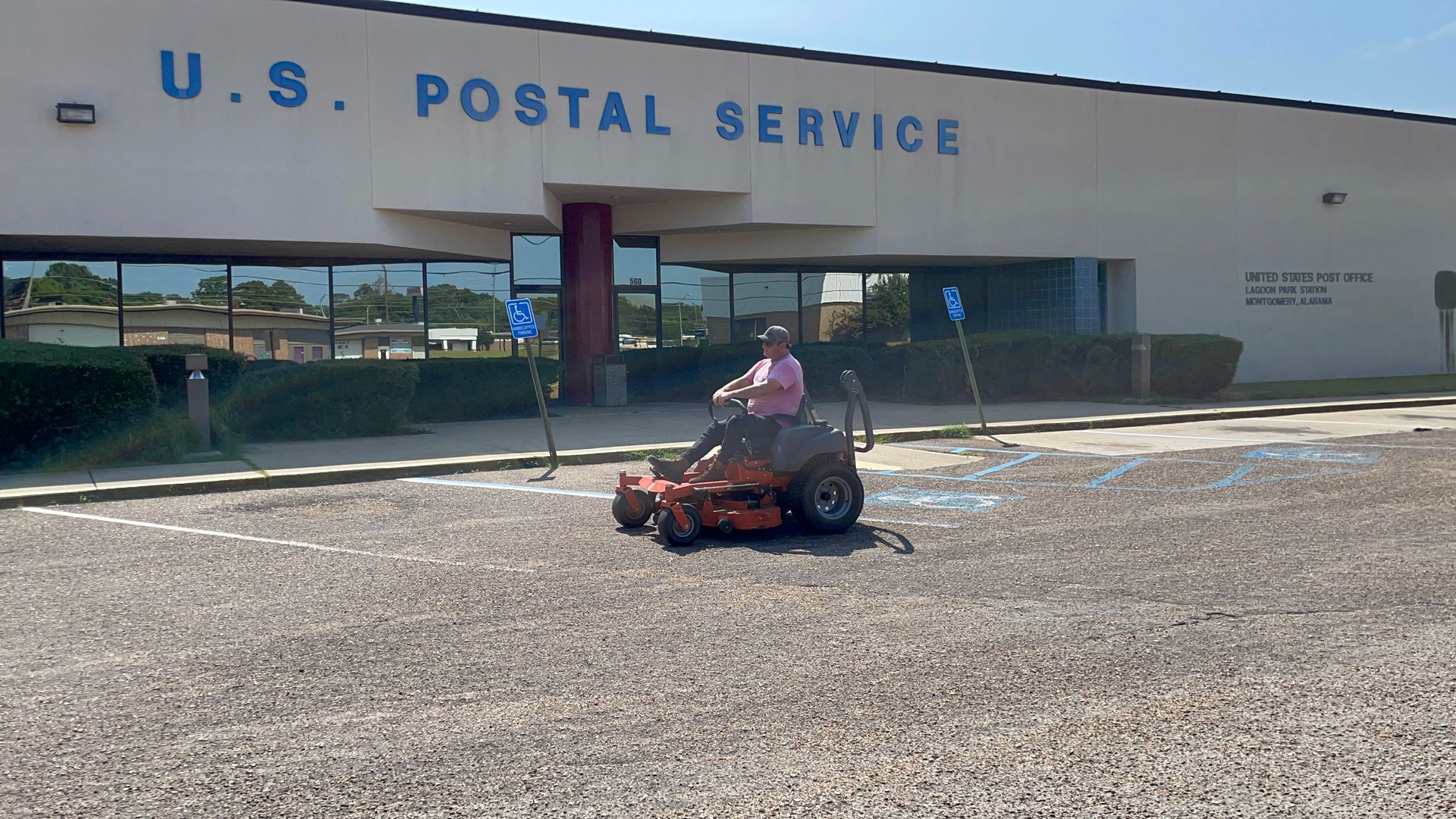 Person on a lawn mower in front of a U.S. Postal Service building