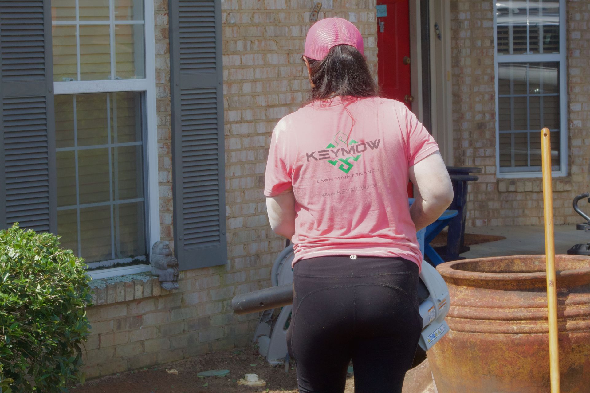 Person in pink cap and shirt working outside near a brick house and stacked planter rings
