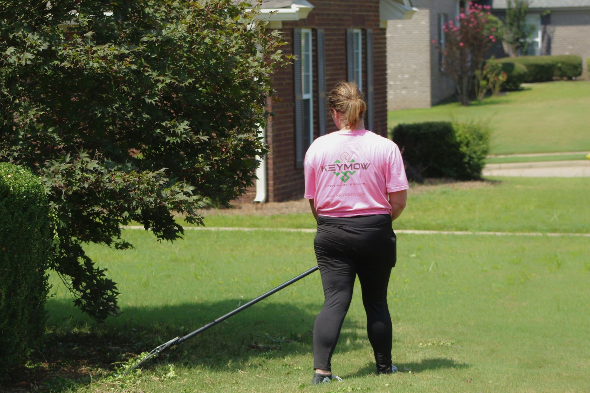 Person in a pink shirt mowing a lawn in a suburban yard