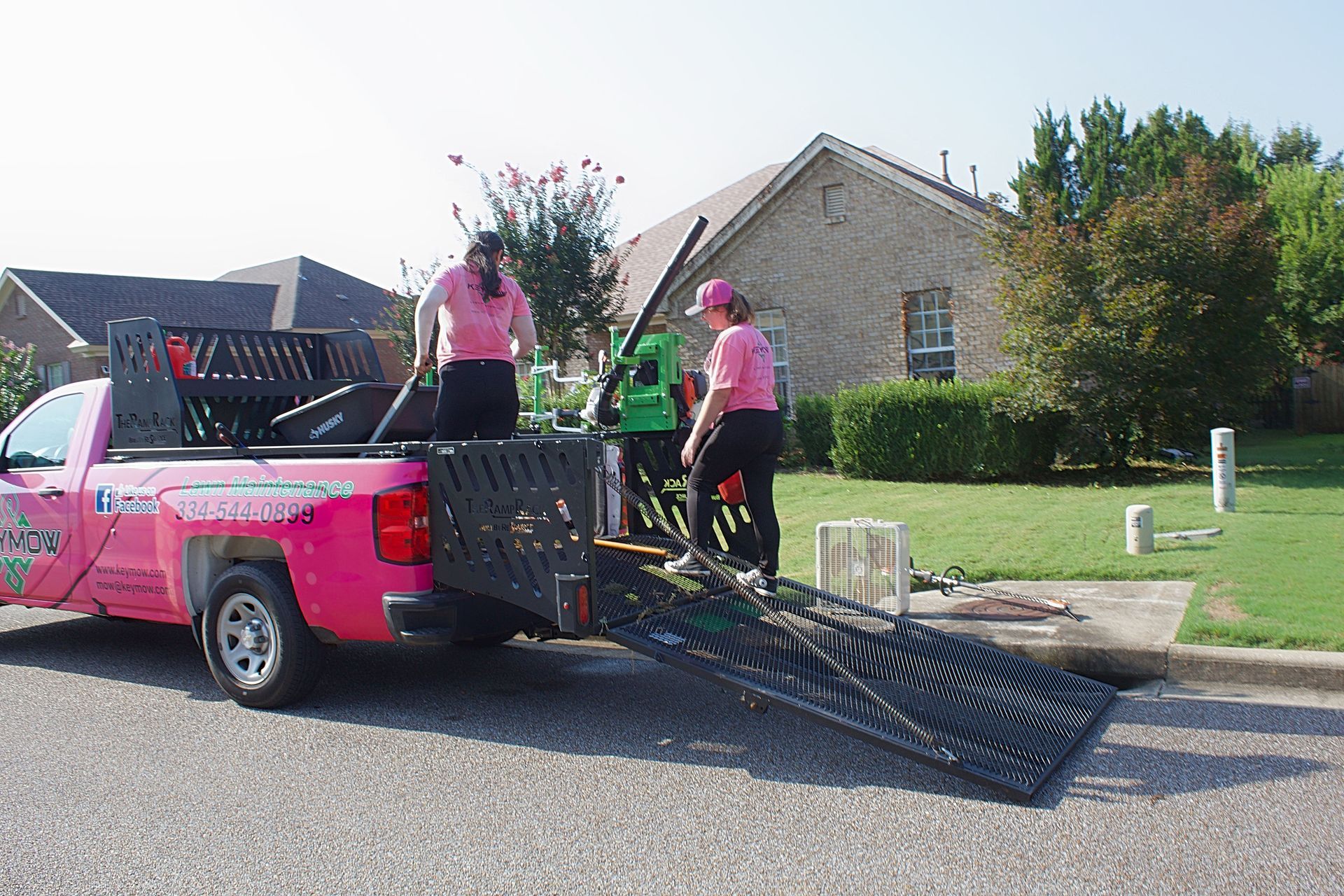 Pink pickup truck parked on street with people unloading long black metal gates in a suburban neighborhood