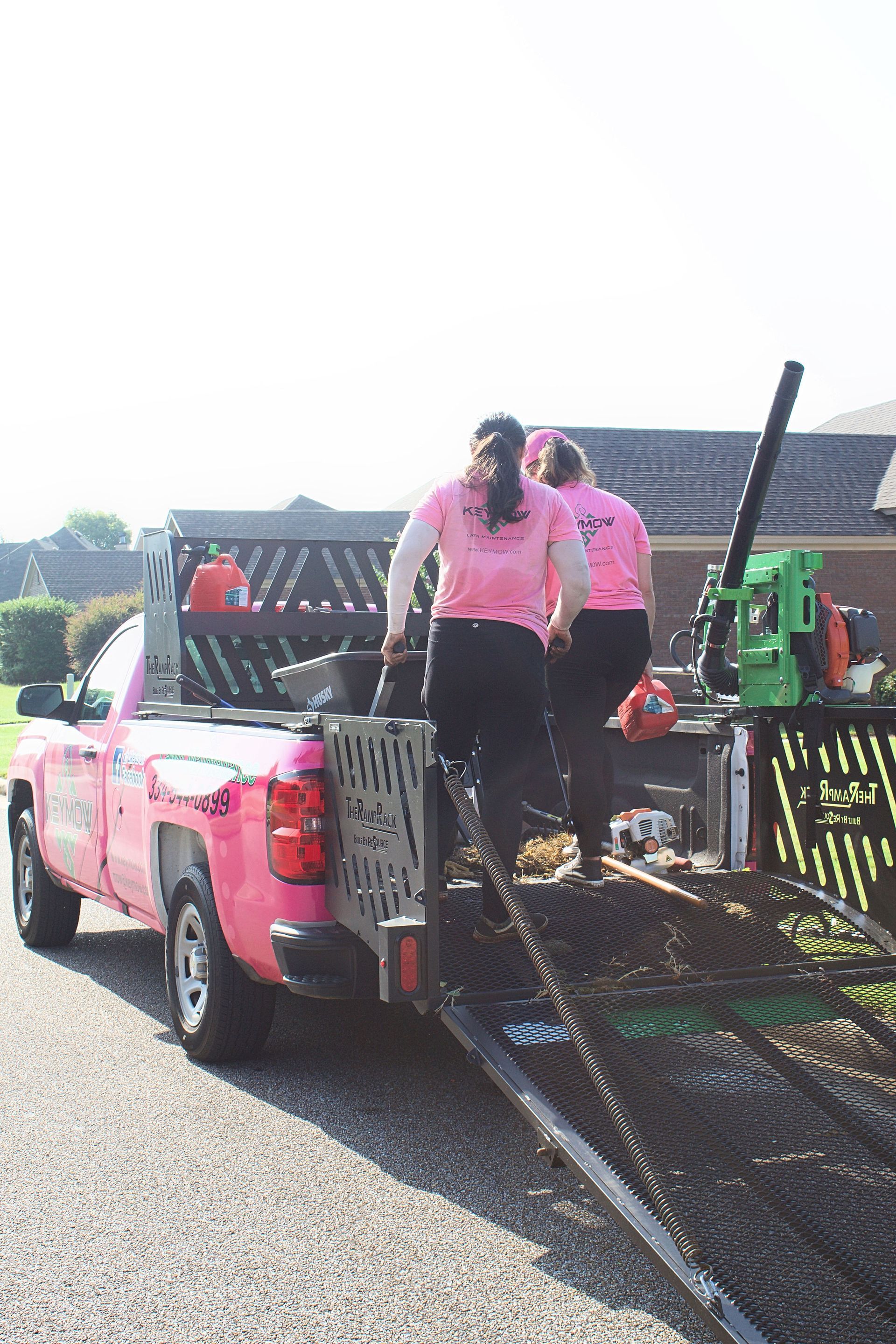 Pink truck on a trailer with two people in pink shirts securing it on a sunny roadside