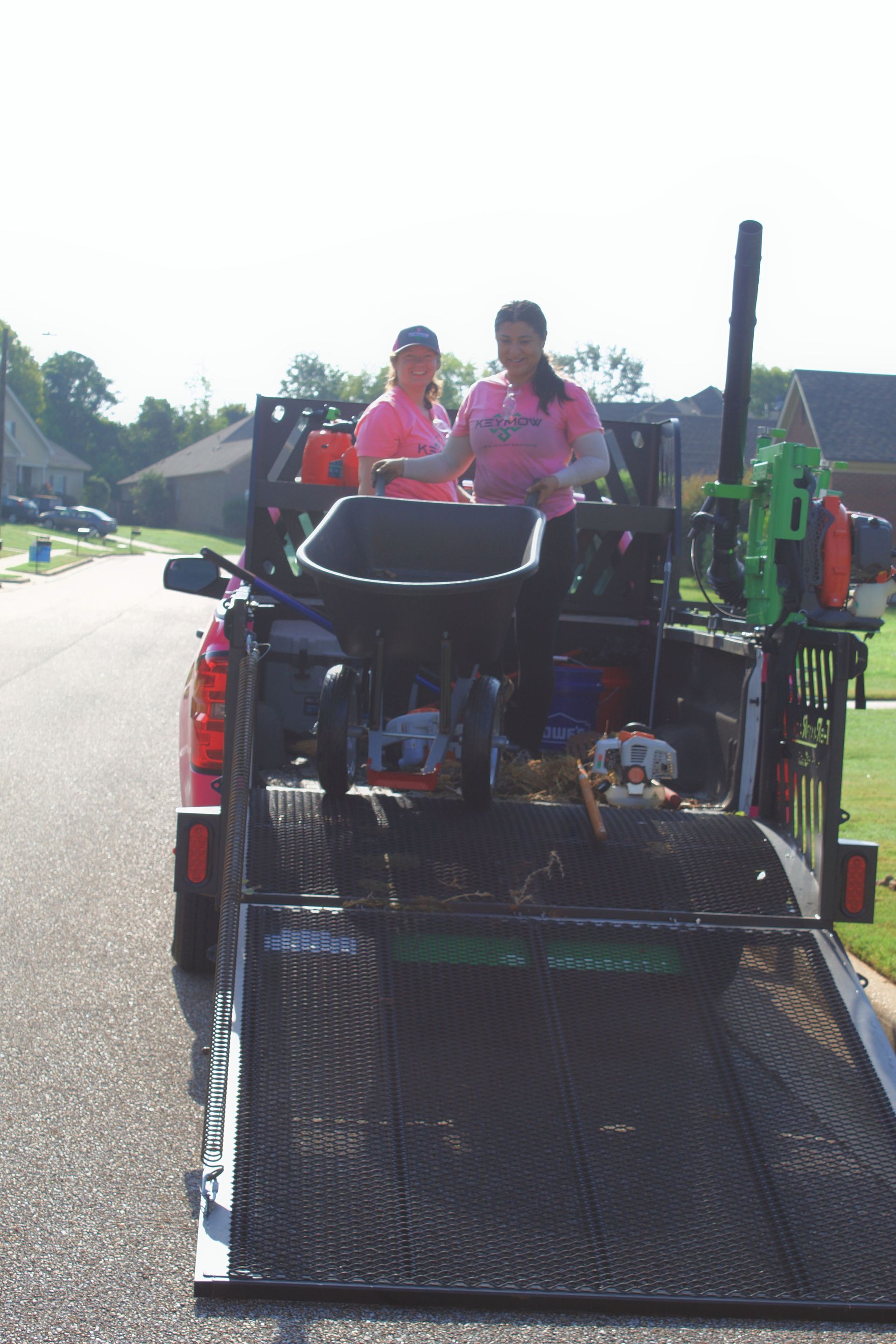Two people in pink shirts riding on a green and black utility vehicle outdoors on a sunny street