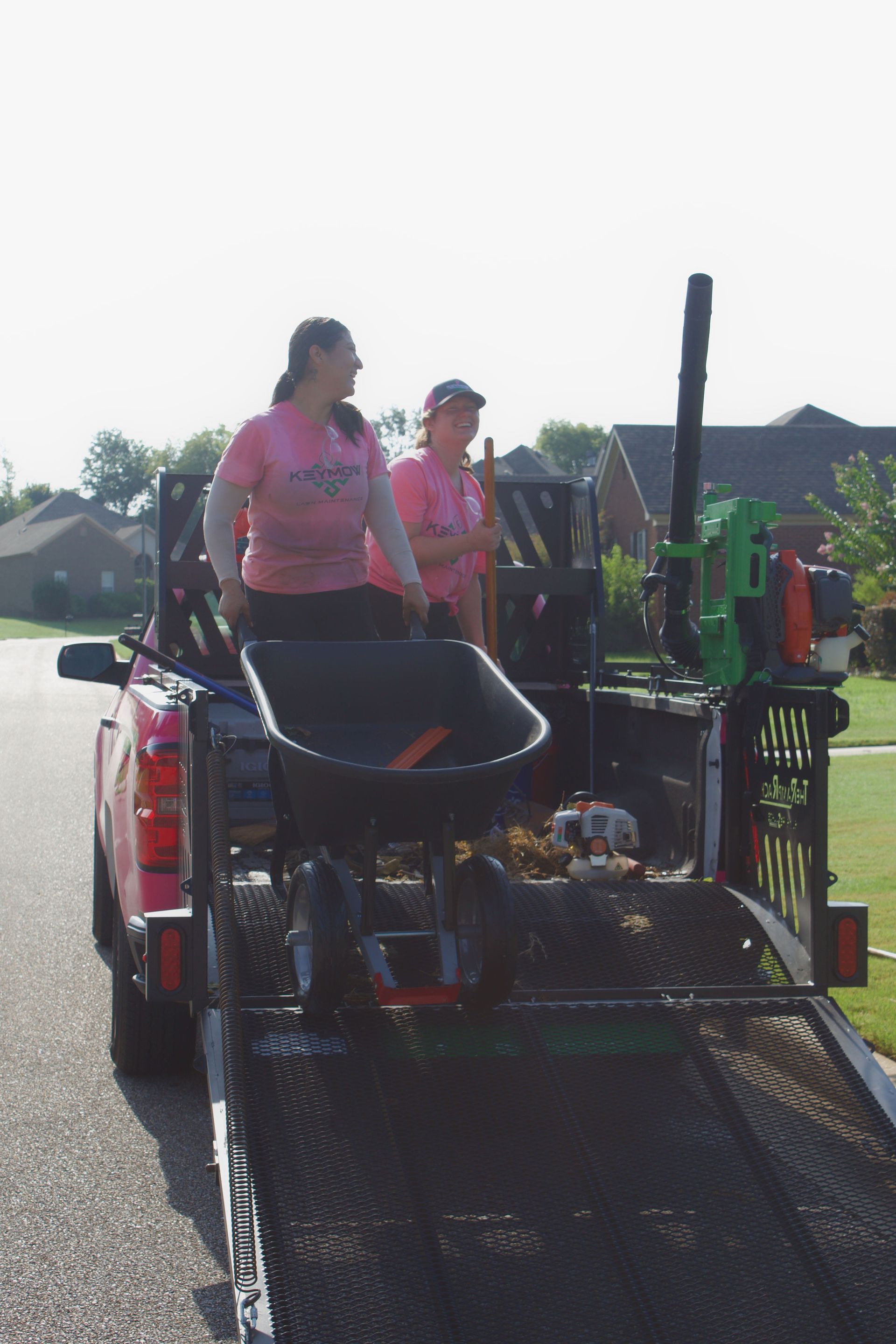 Two workers on a roadside utility machine, wearing safety vests, beside a grassy neighborhood street