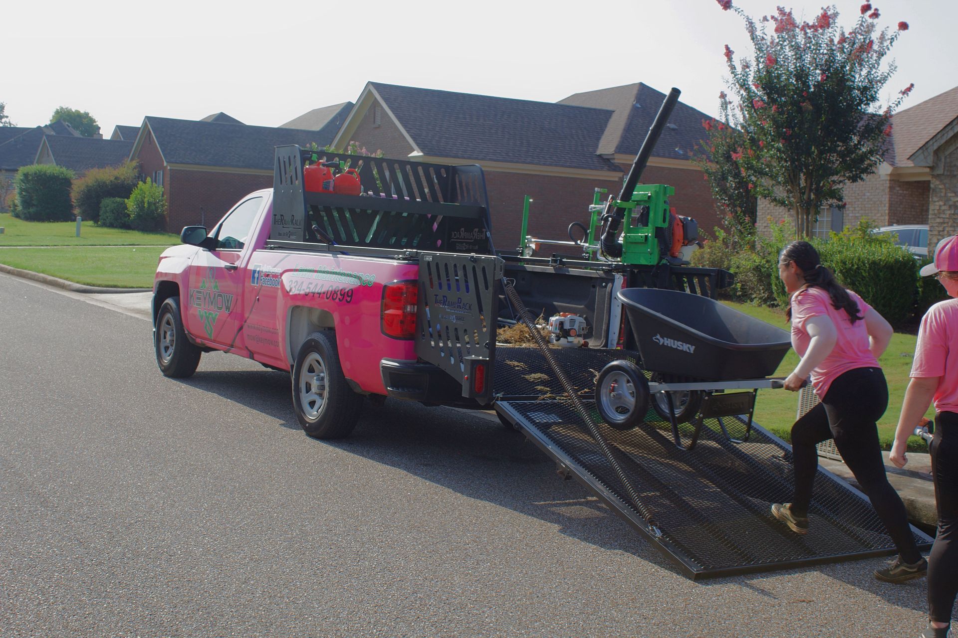 Pink pickup truck hauling a trailer as two people push it on a suburban street