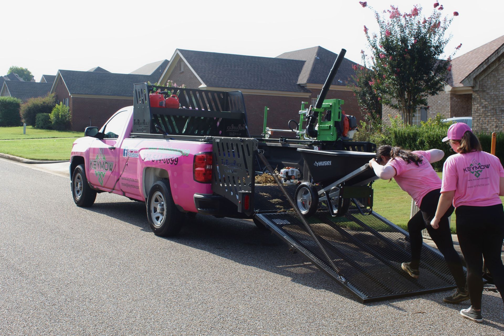 Workers loading metal ramps onto a pink pickup truck in a suburban street