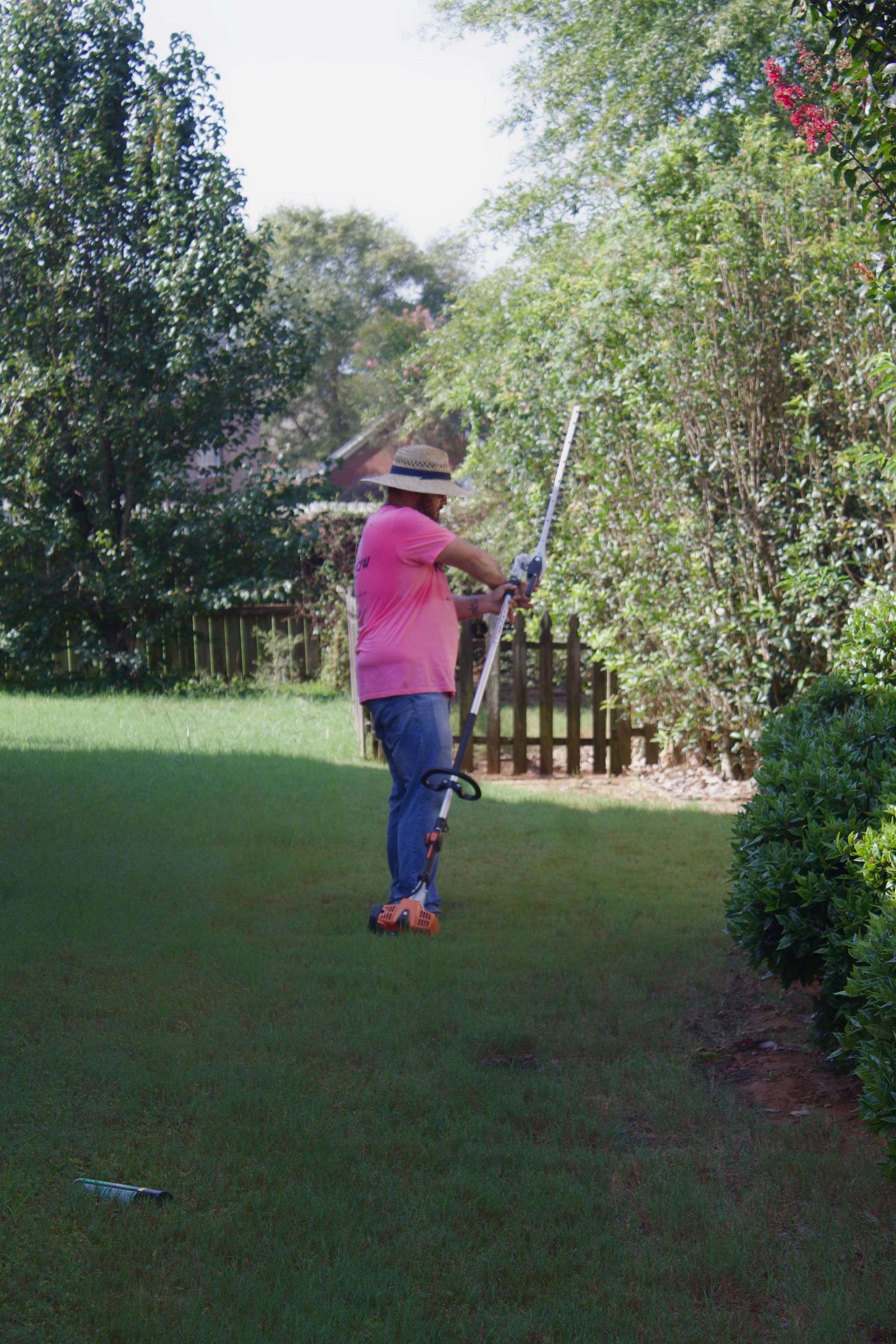 Person in pink shirt swinging a golf club on a grassy lawn, surrounded by trees.