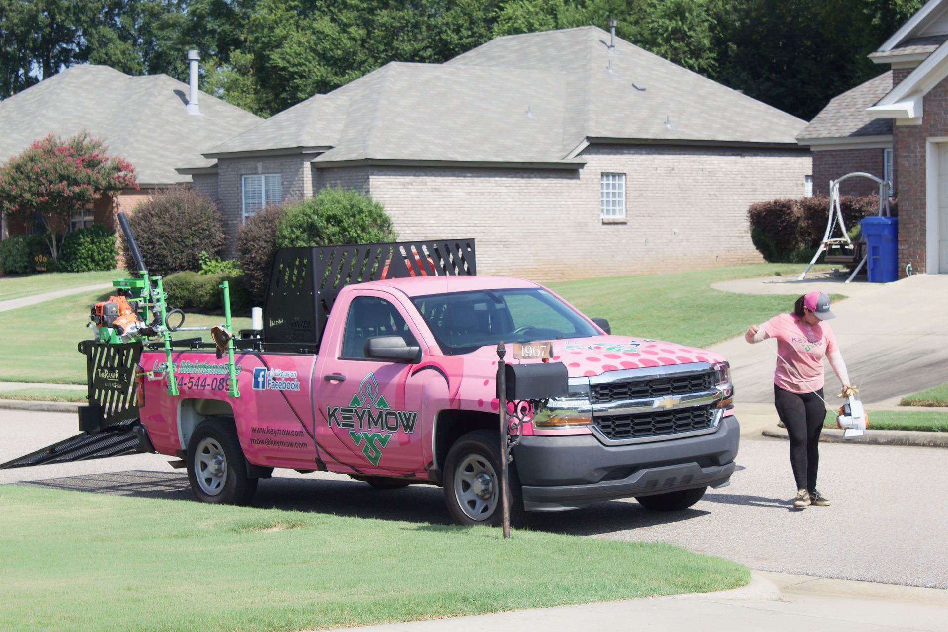 Pink work truck parked on a suburban street while workers unload equipment in front of houses