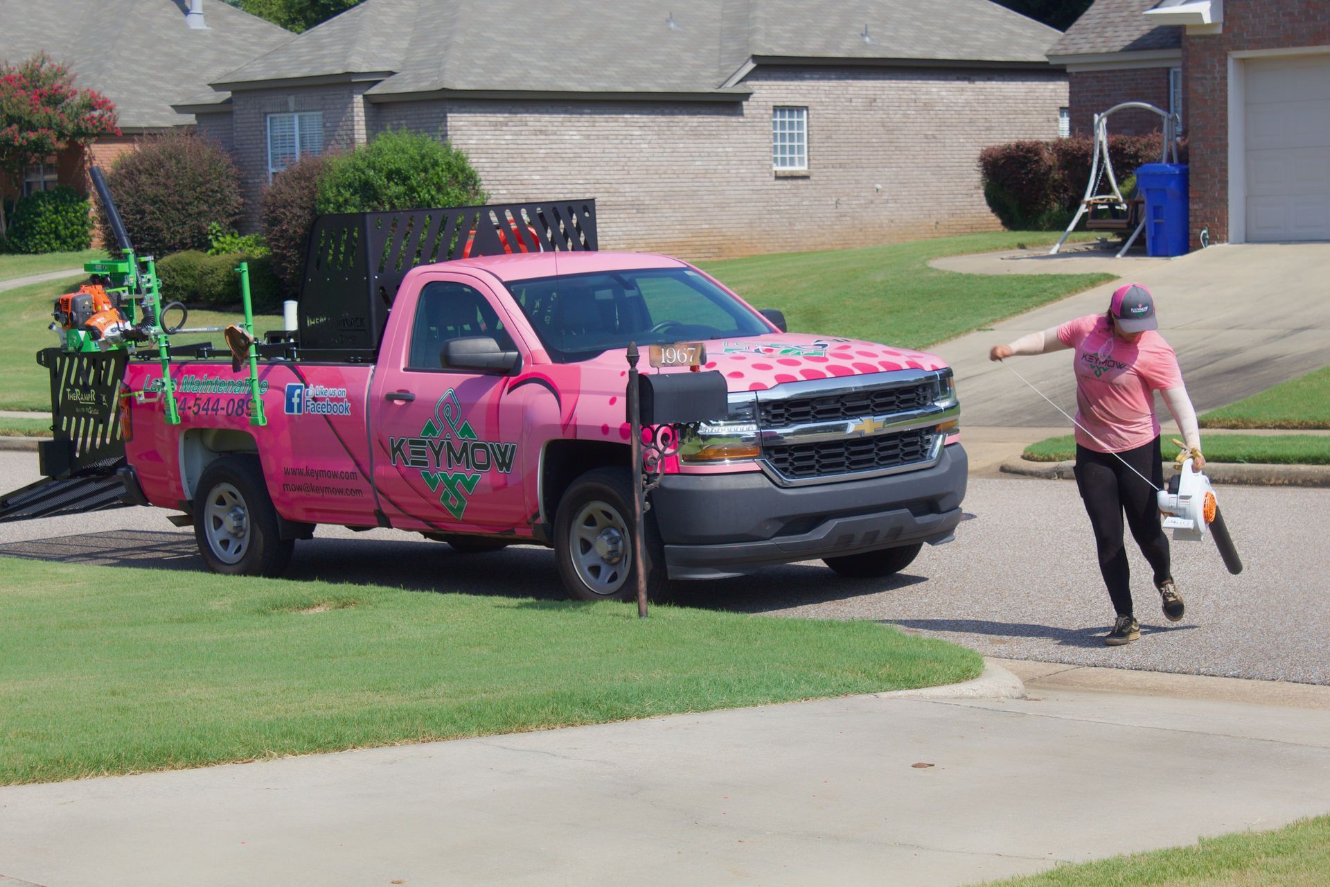 Pink pickup truck parked on a suburban street as a person walks away carrying a bag and bottle.