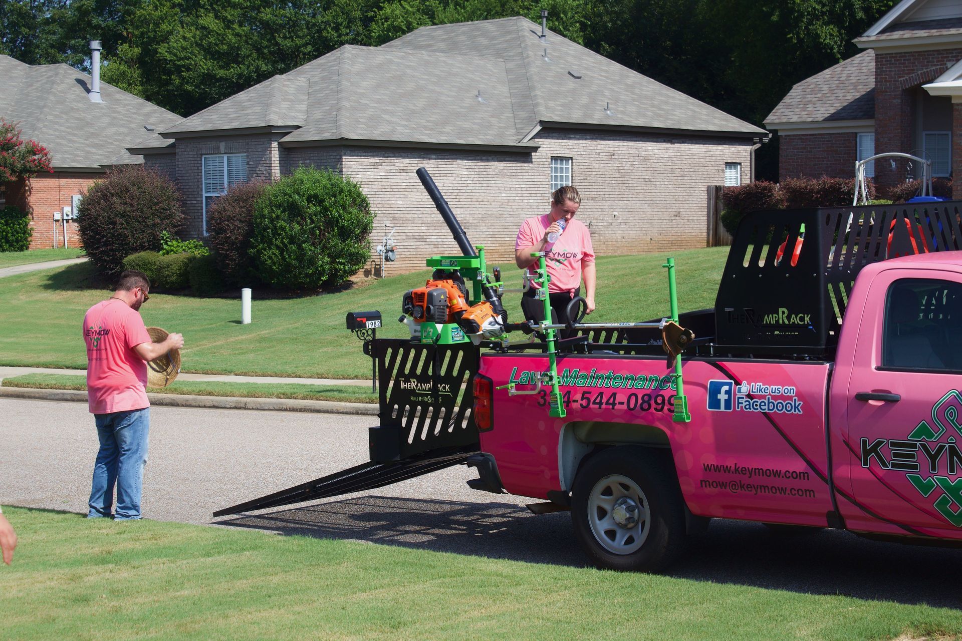 Pink landscaping truck with equipment parked on a suburban street while two people work nearby