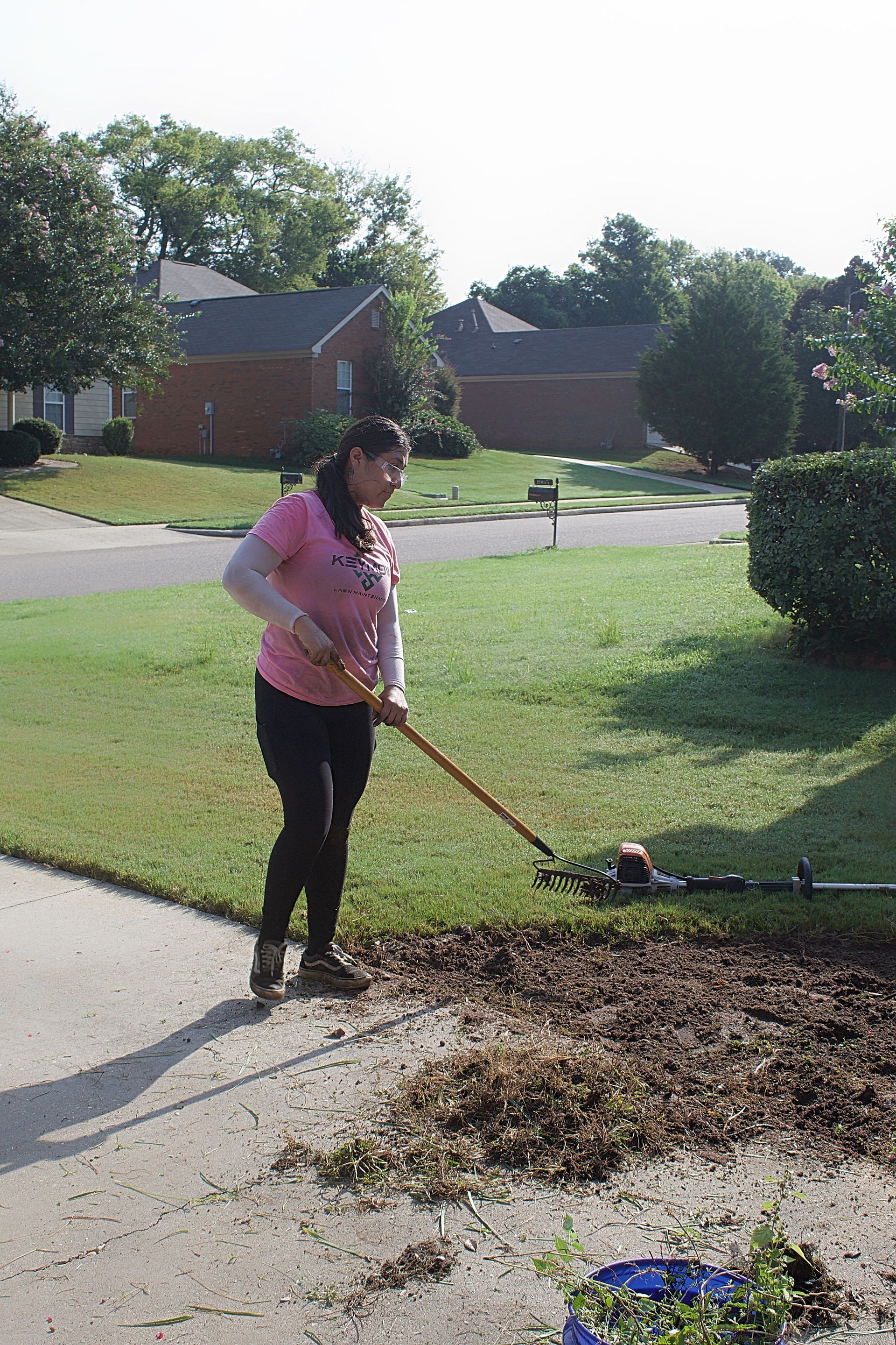 Person raking leaves on a sidewalk beside a lawn in a suburban neighborhood
