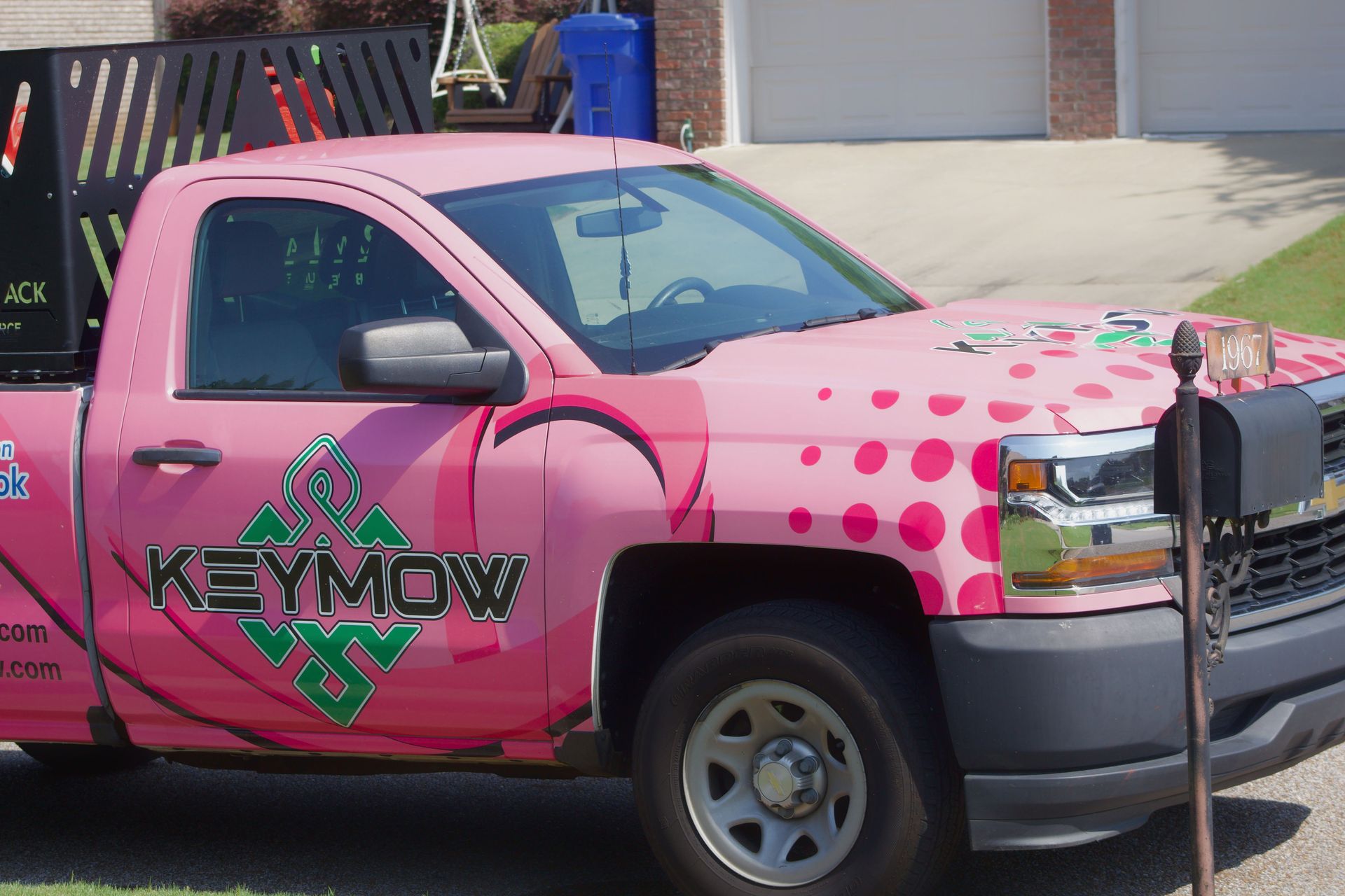 Pink pickup truck with “KEYMOV” logo and polka dots parked outdoors at a driveway.