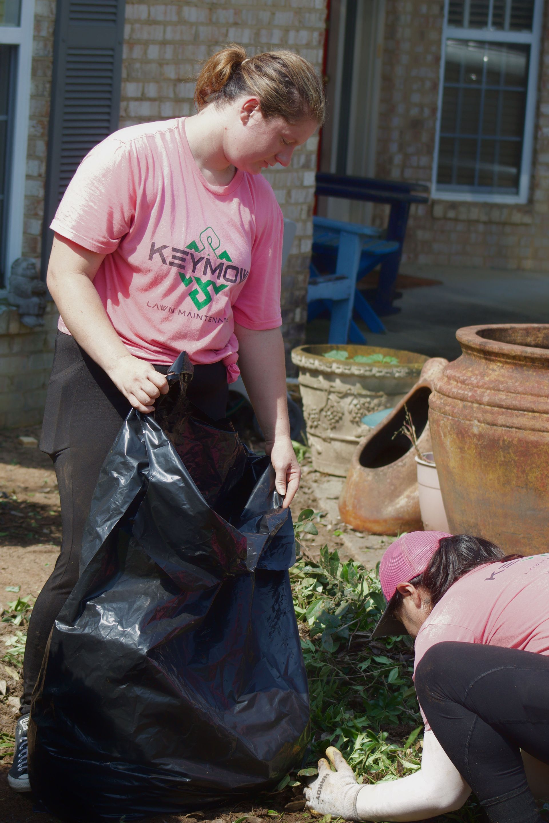 People bagging garden debris beside large clay pots outside a building