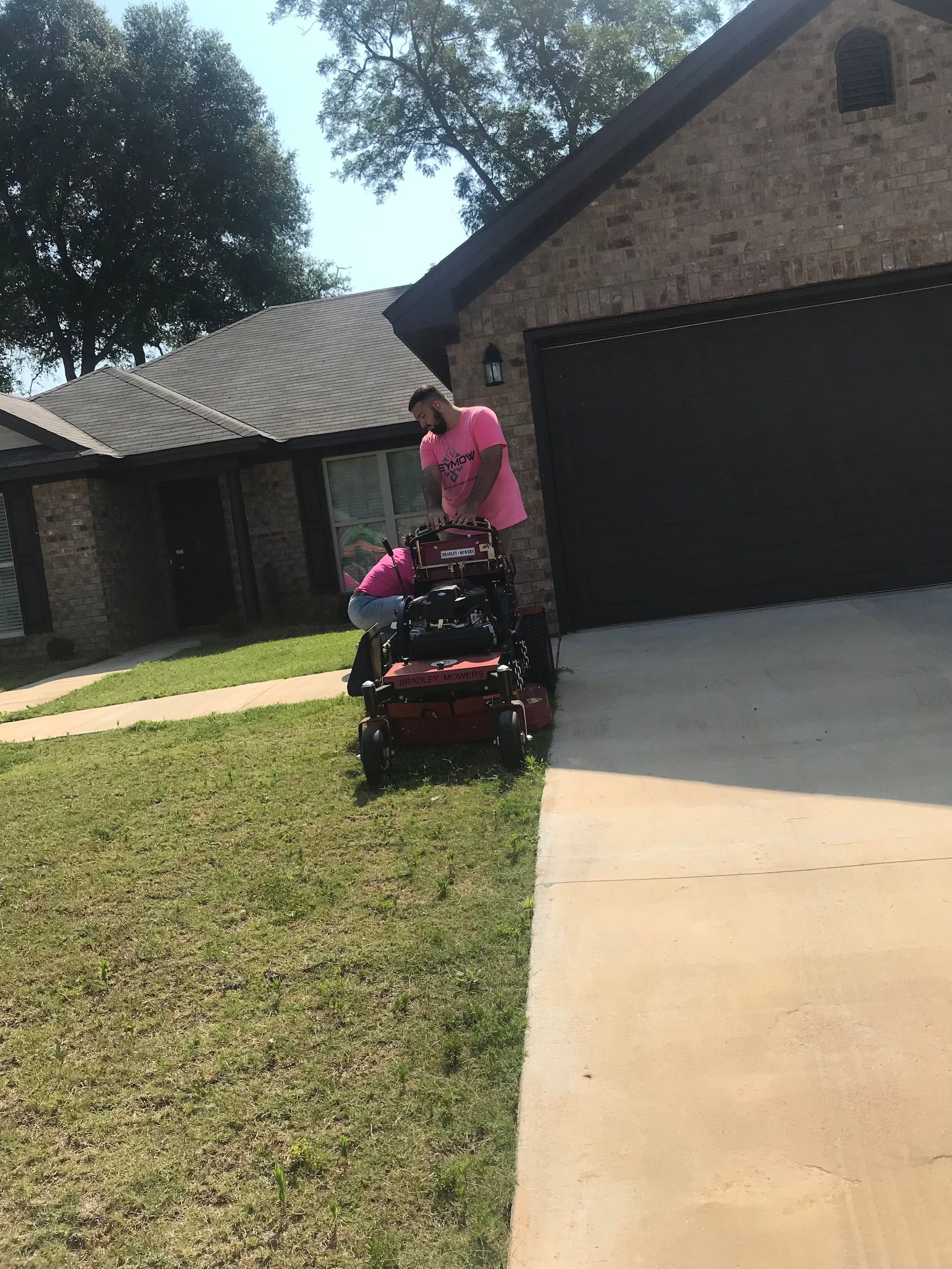 Person standing behind a pink stroller on a lawn beside a driveway and brick house