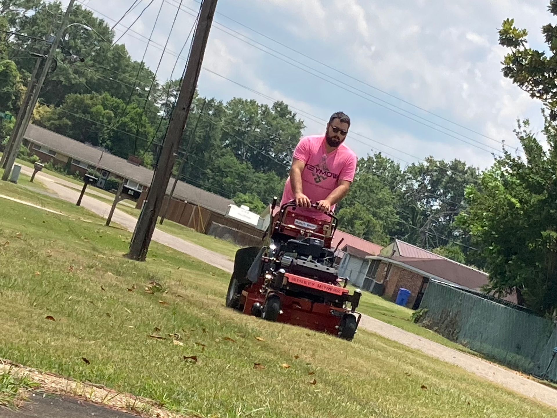 Person in a pink shirt riding a red lawn mower across a grassy field.