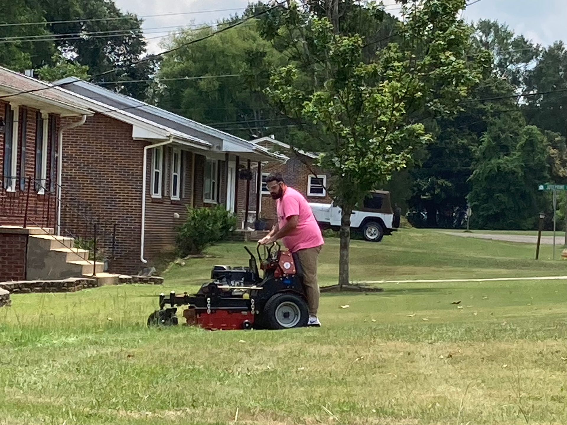 Person mowing a lawn beside a brick house on a sunny day