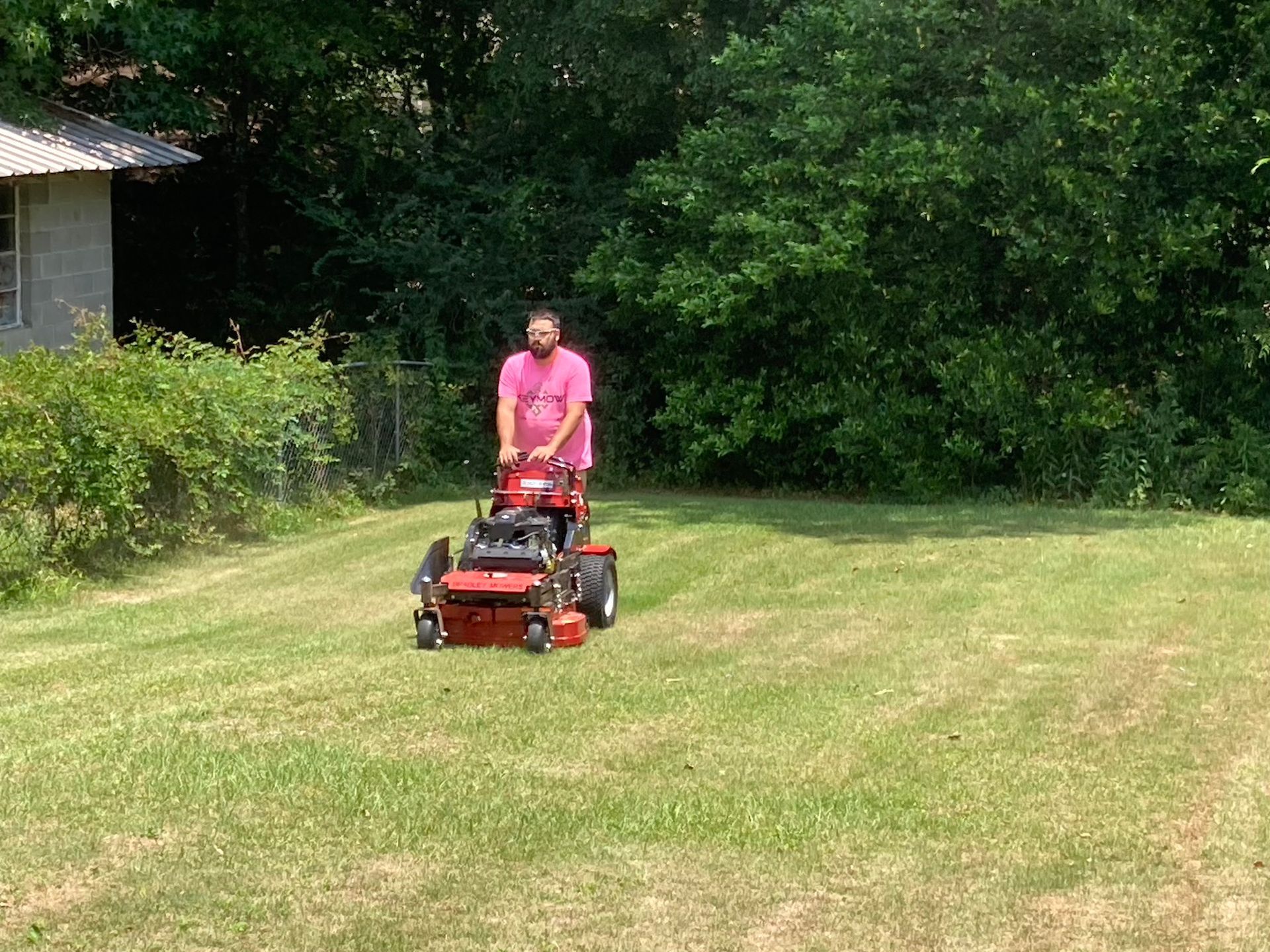 Person riding a red lawn mower across a grassy yard near trees and a house