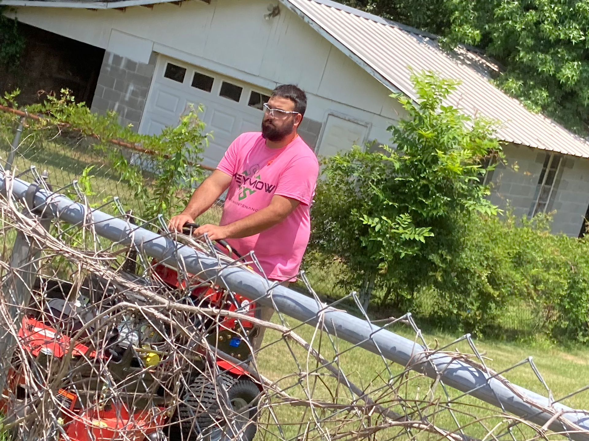 Man on a red ATV beside a chain-link fence in a grassy yard, with a house in the background.