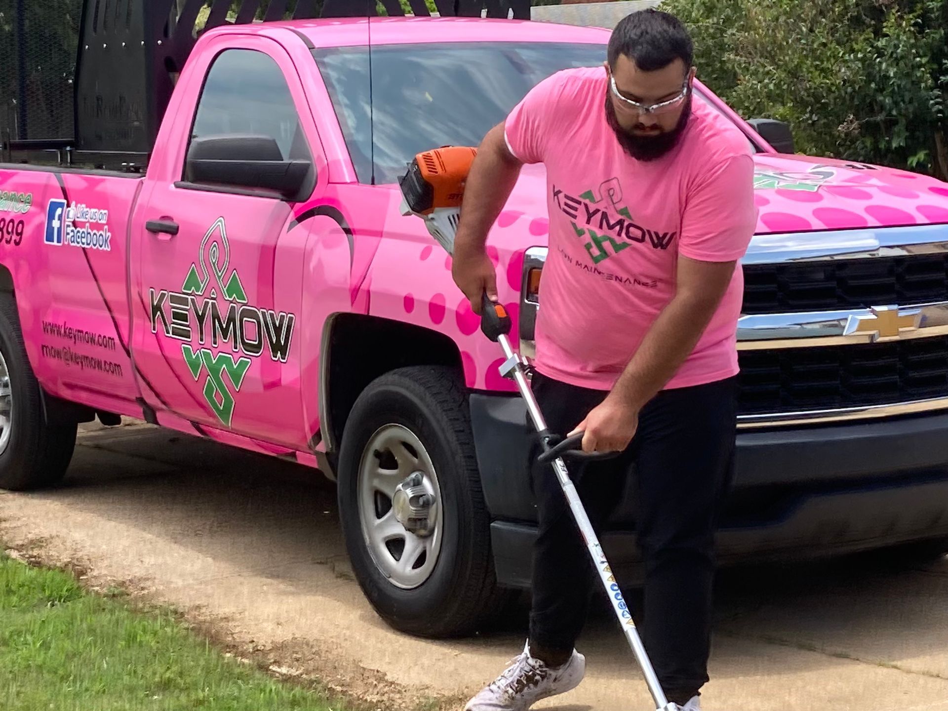 Man in pink shirt using a string trimmer beside a pink pickup truck on a driveway