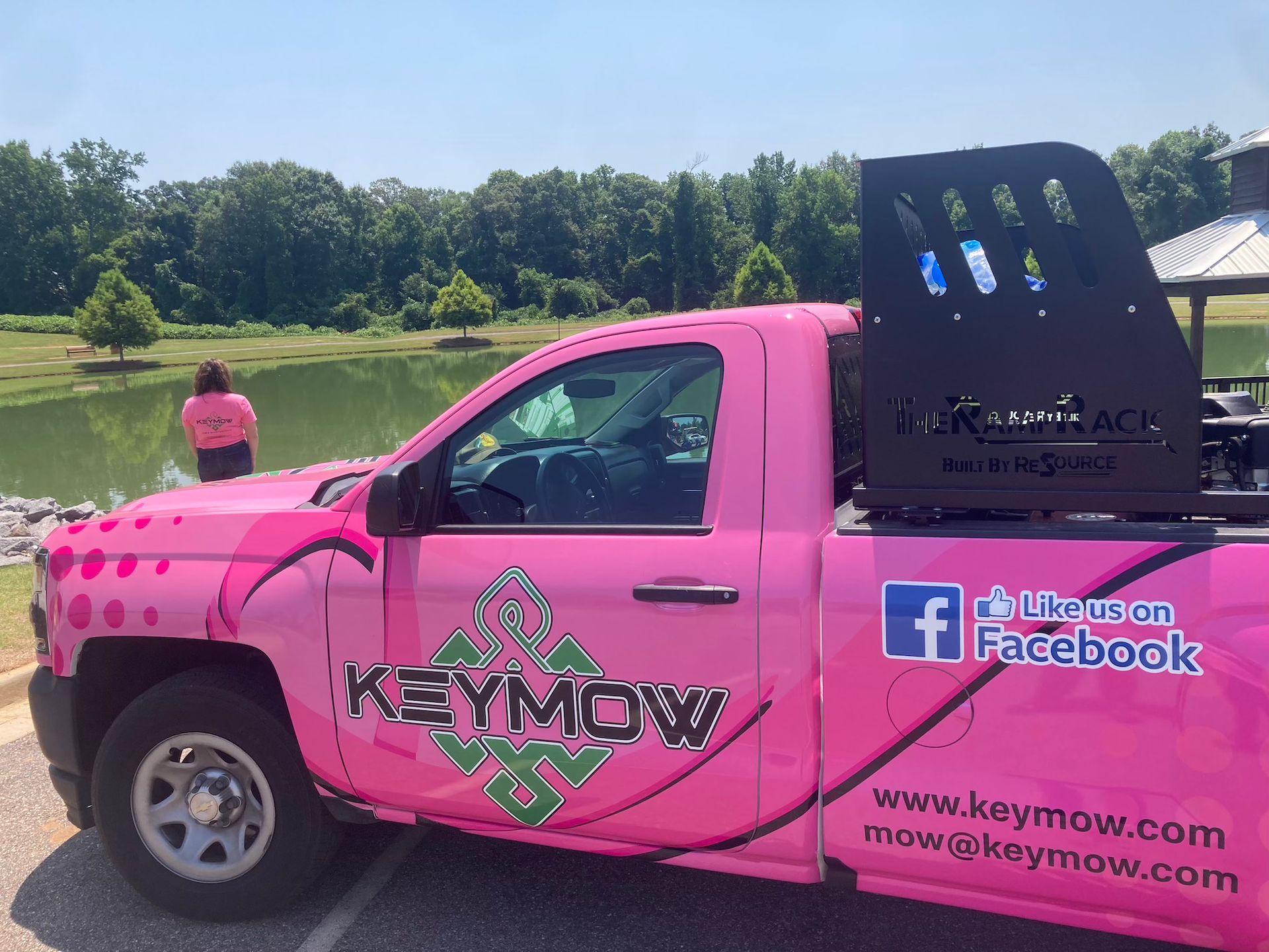 Bright pink Keymow pickup truck parked by a lake, with Facebook branding and a black tool rack in back