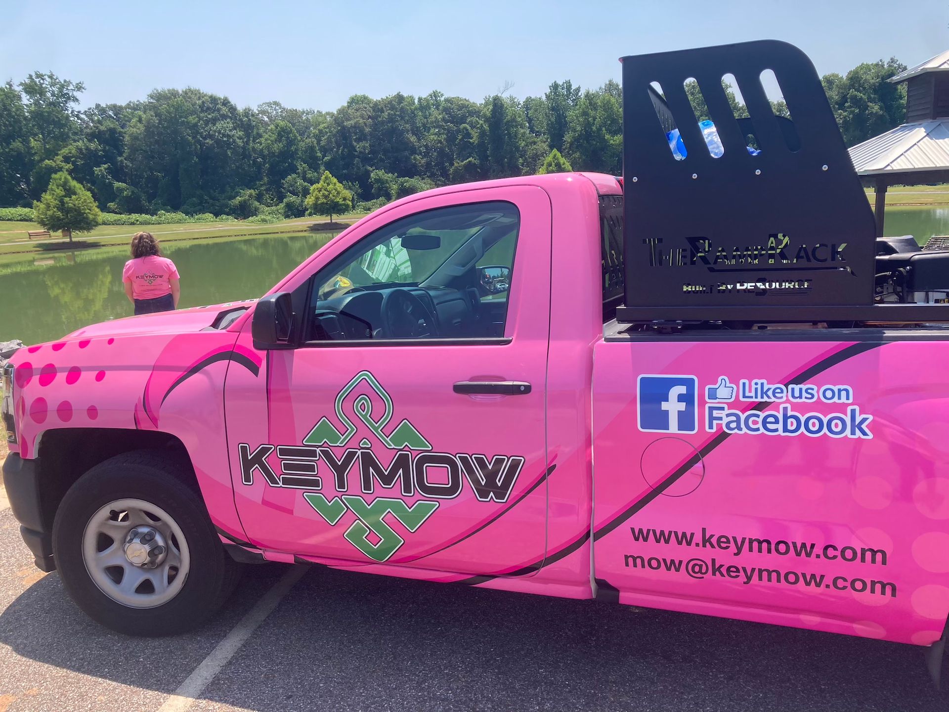 Pink KIMOW pickup truck with Facebook branding parked outdoors on a sunny field