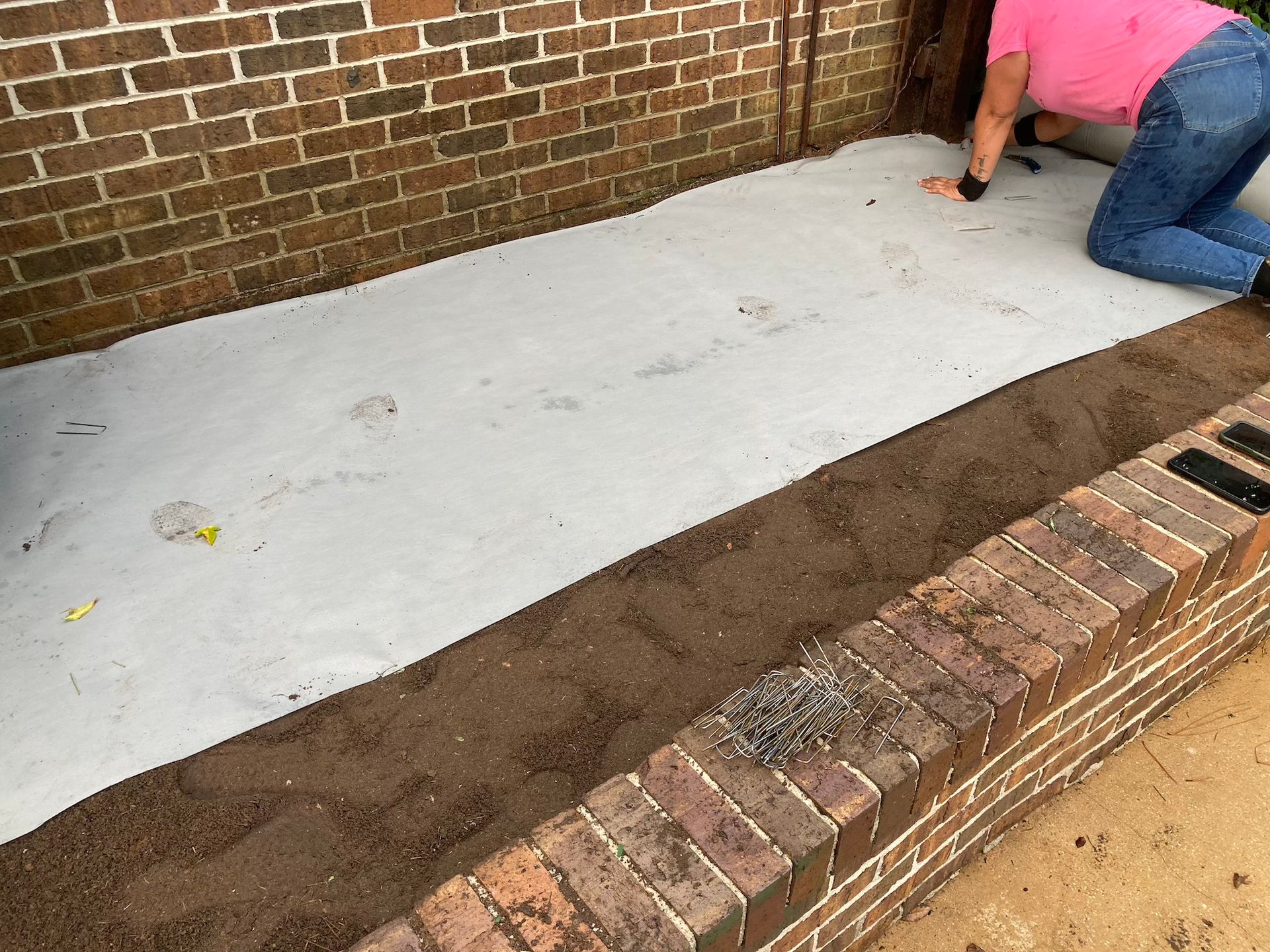 Person kneeling by a brick wall, smoothing fresh concrete in a narrow outdoor walkway