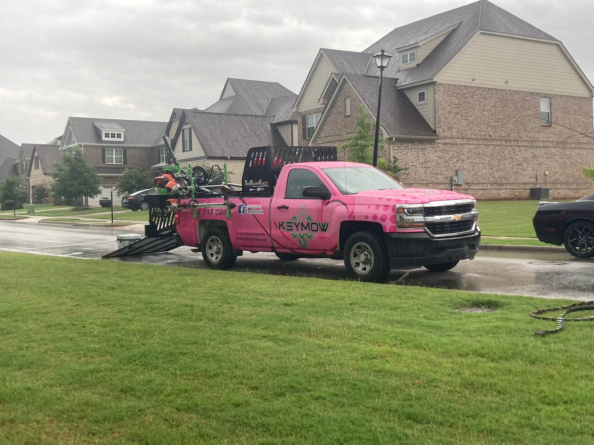 Bright pink tow truck with floral graphics parked in a suburban neighborhood after rain