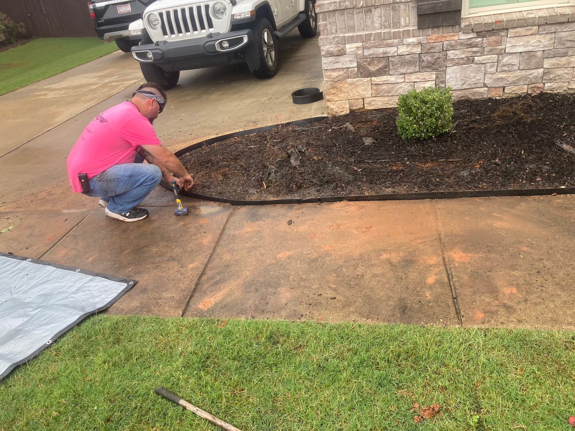 Worker in pink shirt kneeling to repair a cracked concrete driveway beside a house