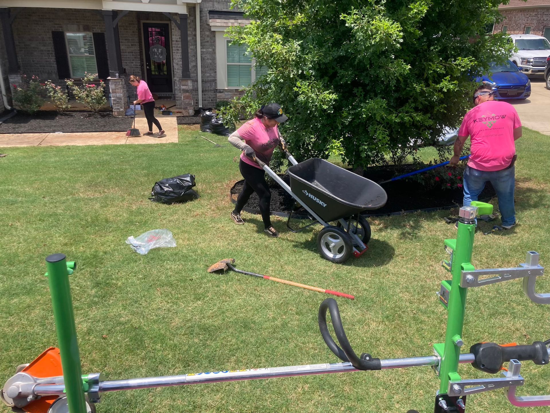 People moving a wheelbarrow and working in a yard beside green exercise equipment.