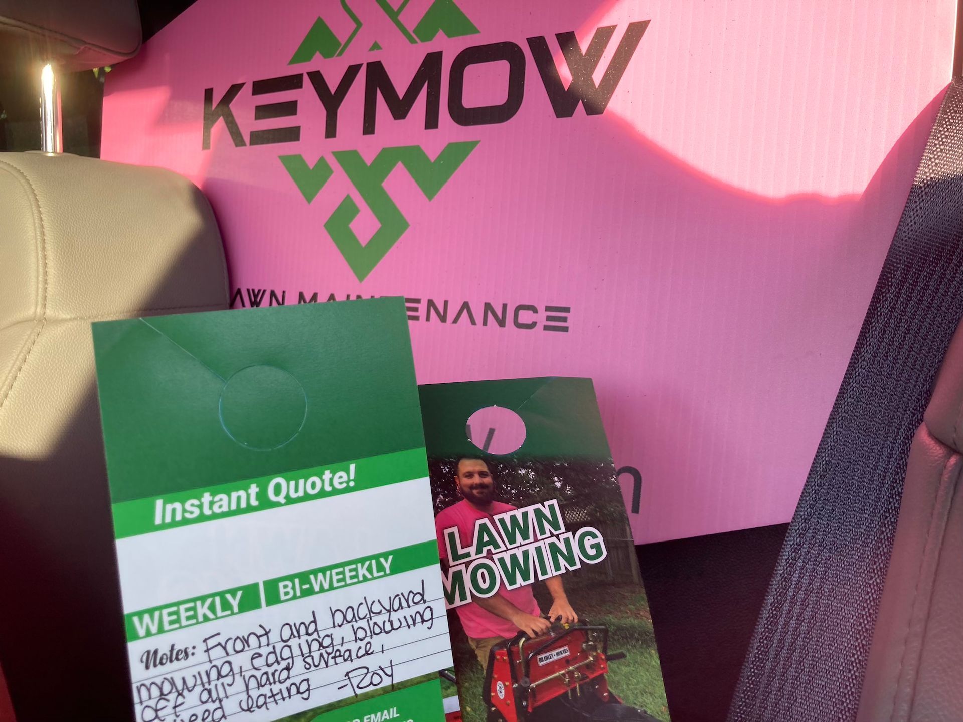 Green lawn care flyers on a car seat in front of a pink Keymow maintenance sign