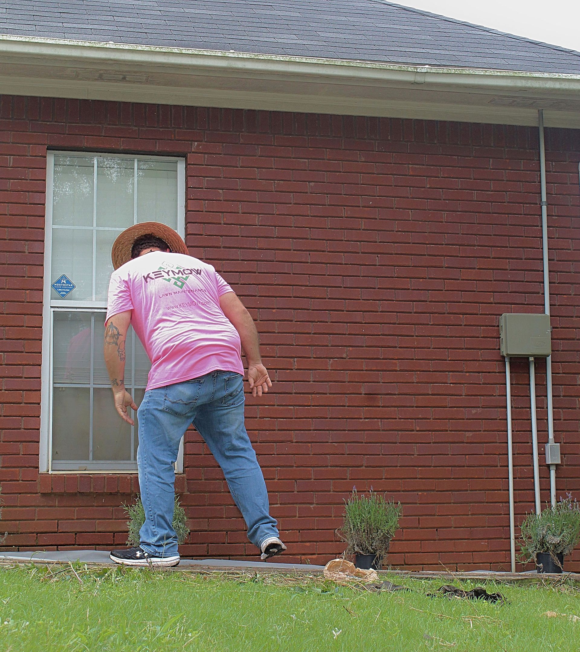 Person leaning near a brick house window beside a small garden