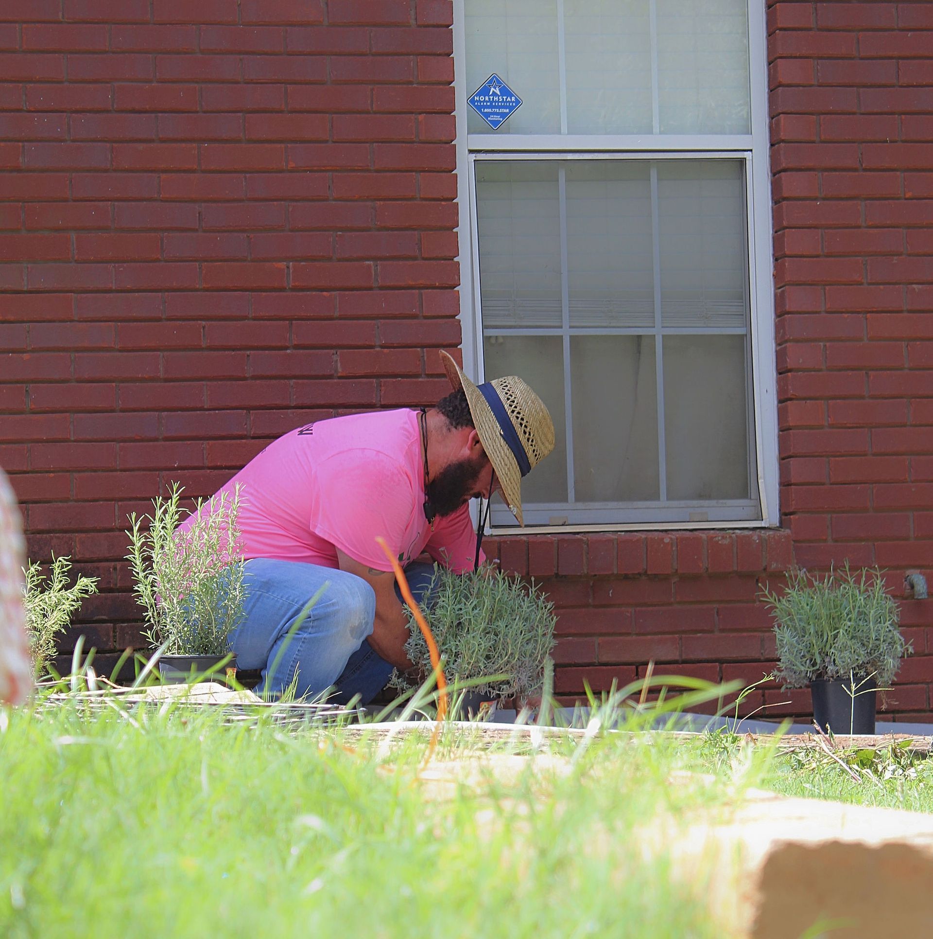 Person kneeling to tend plants beside a red brick house window