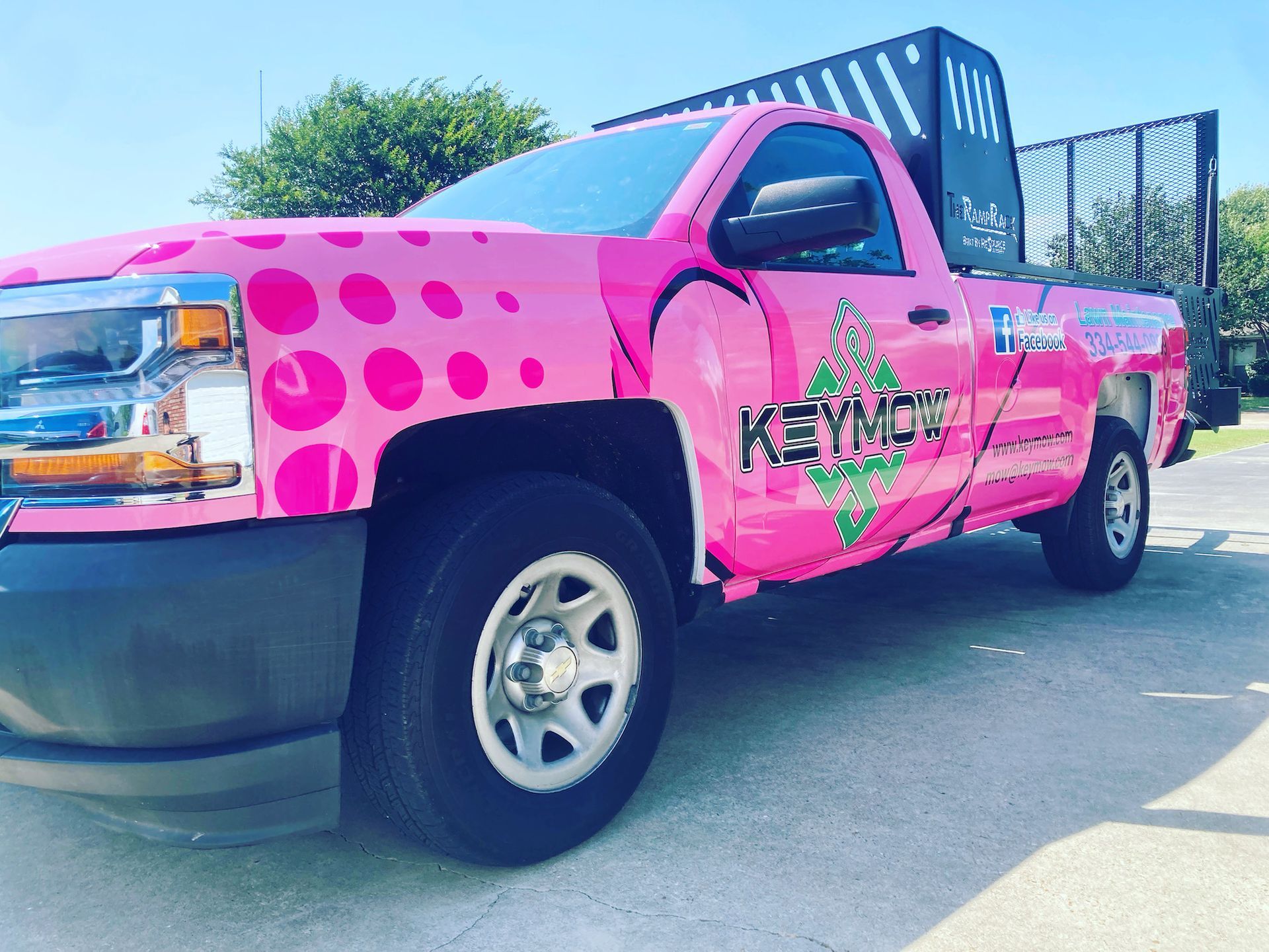 Bright pink polka-dot pickup truck with custom graphics parked outdoors near a fence